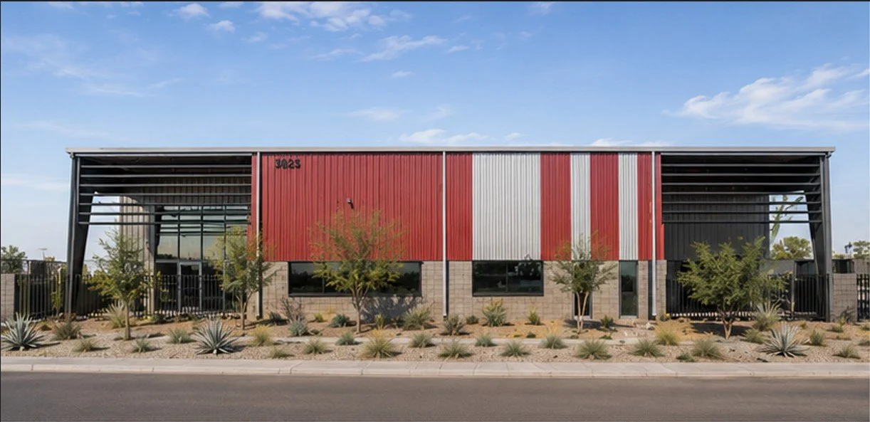 Modern industrial building with red and white metal siding, black metal framework, and desert landscaping with small trees and succulents in front.