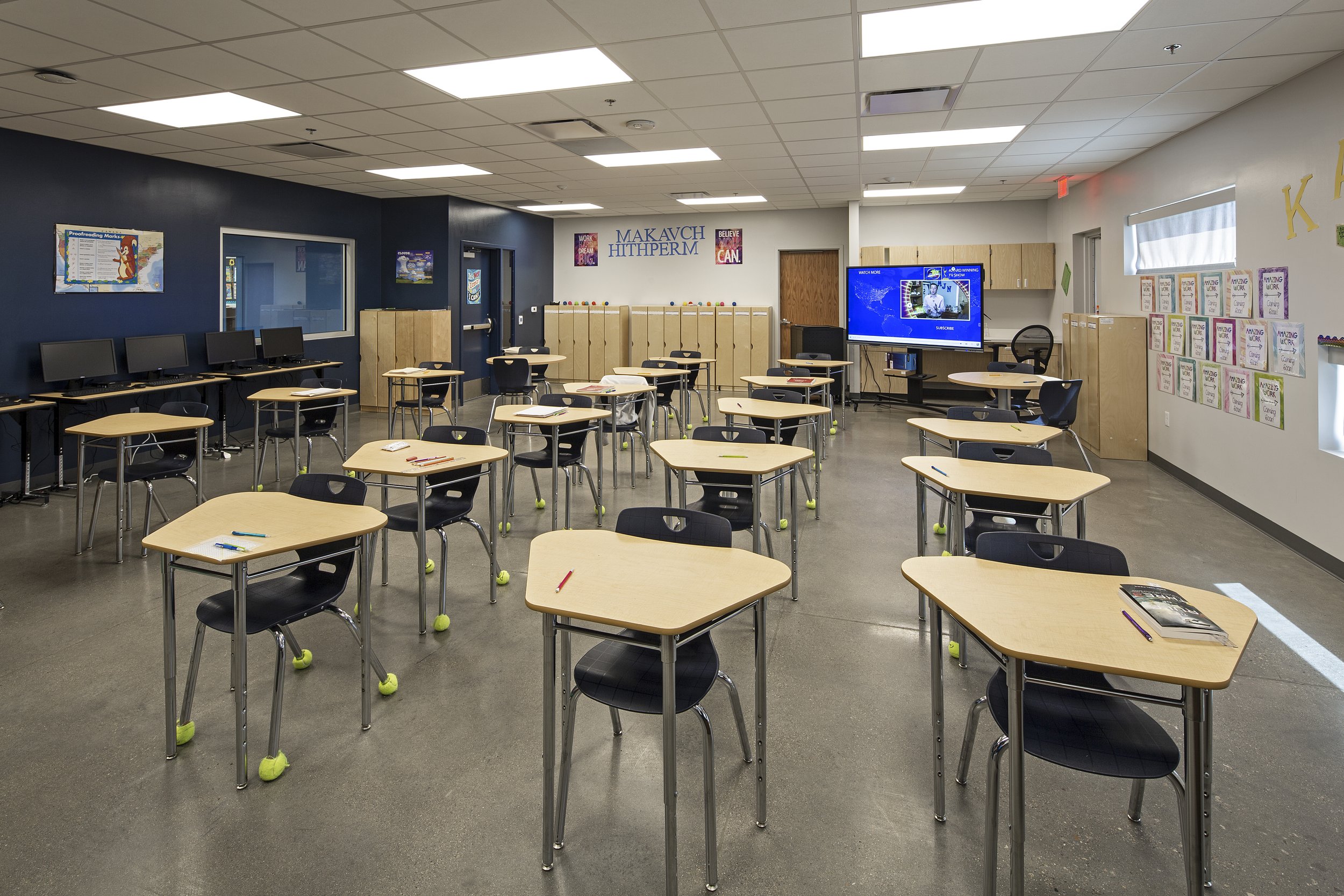 Empty classroom with desks and chairs, monitor at the front, and colorful posters on the walls.