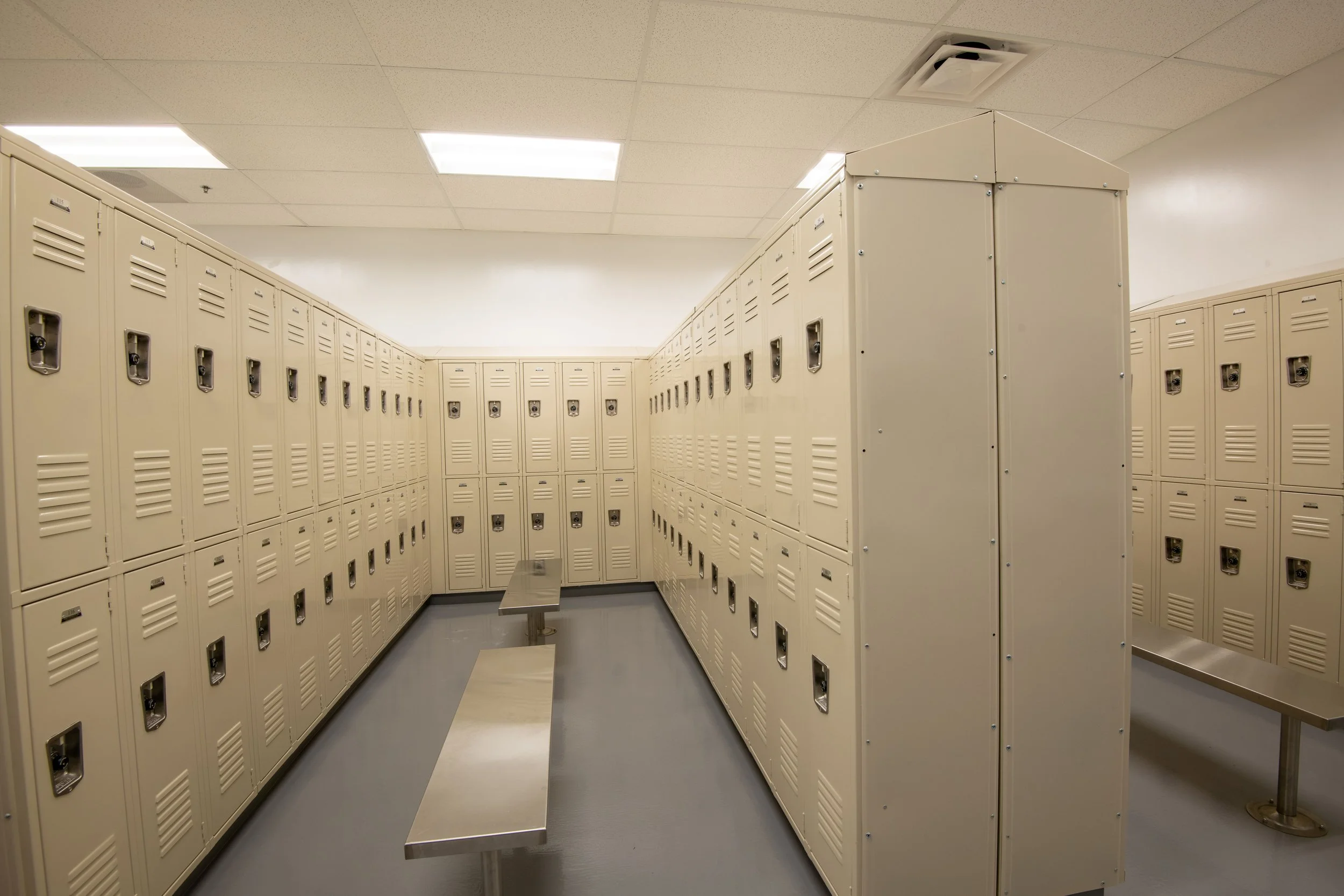 Locker room with beige metal lockers and metal benches.