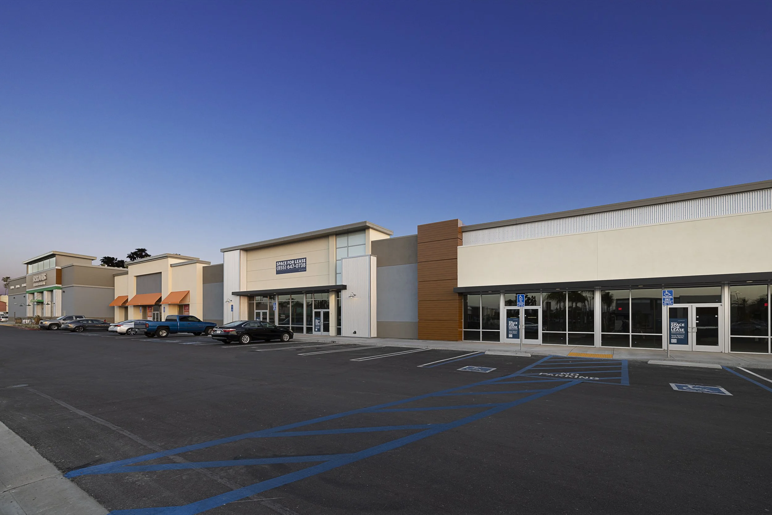 Empty parking lot in front of a shopping center with a clear blue sky overhead.