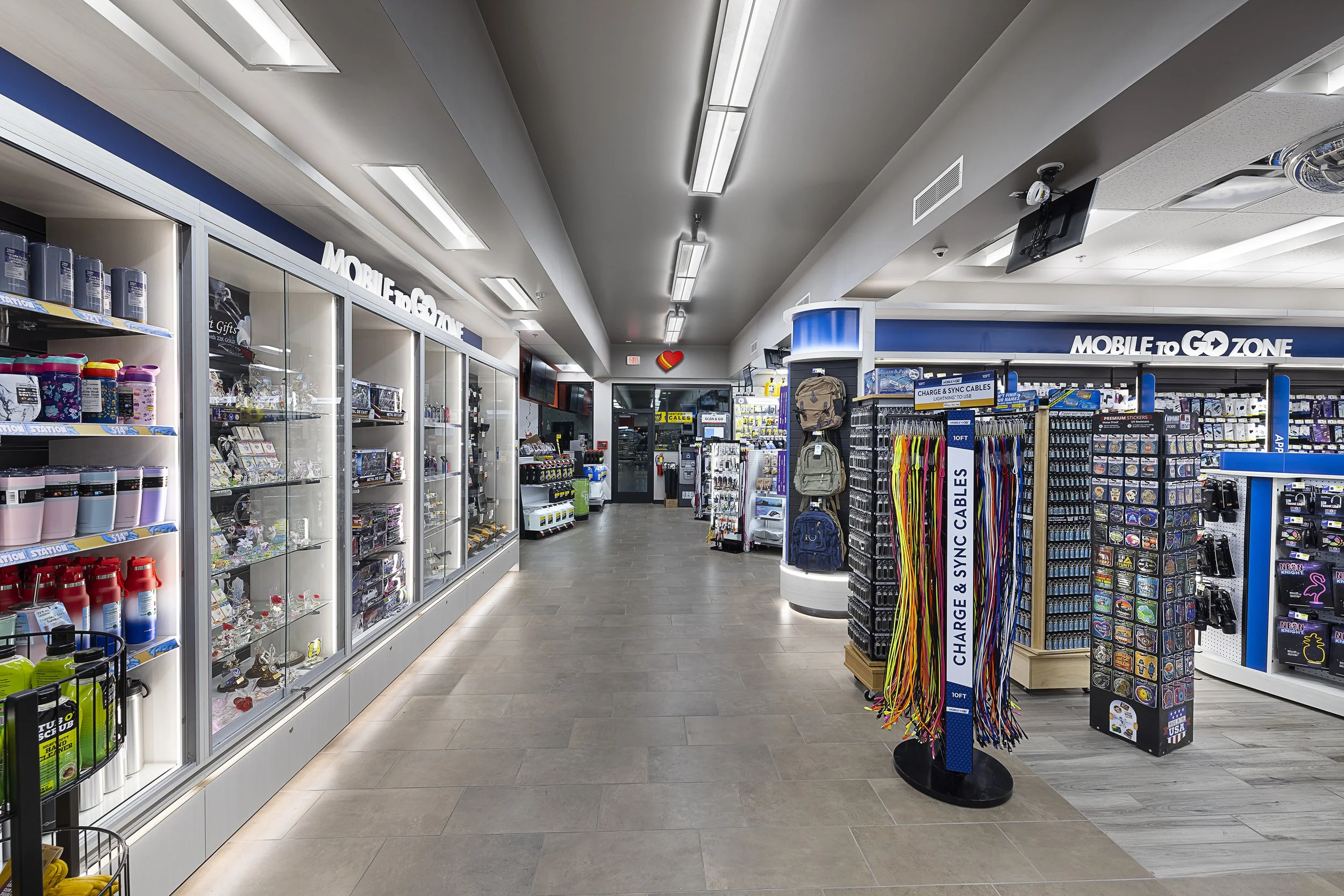 Inside a retail store with shelves stocked with various electronic accessories, backpacks, and charging cables, under bright fluorescent lighting.