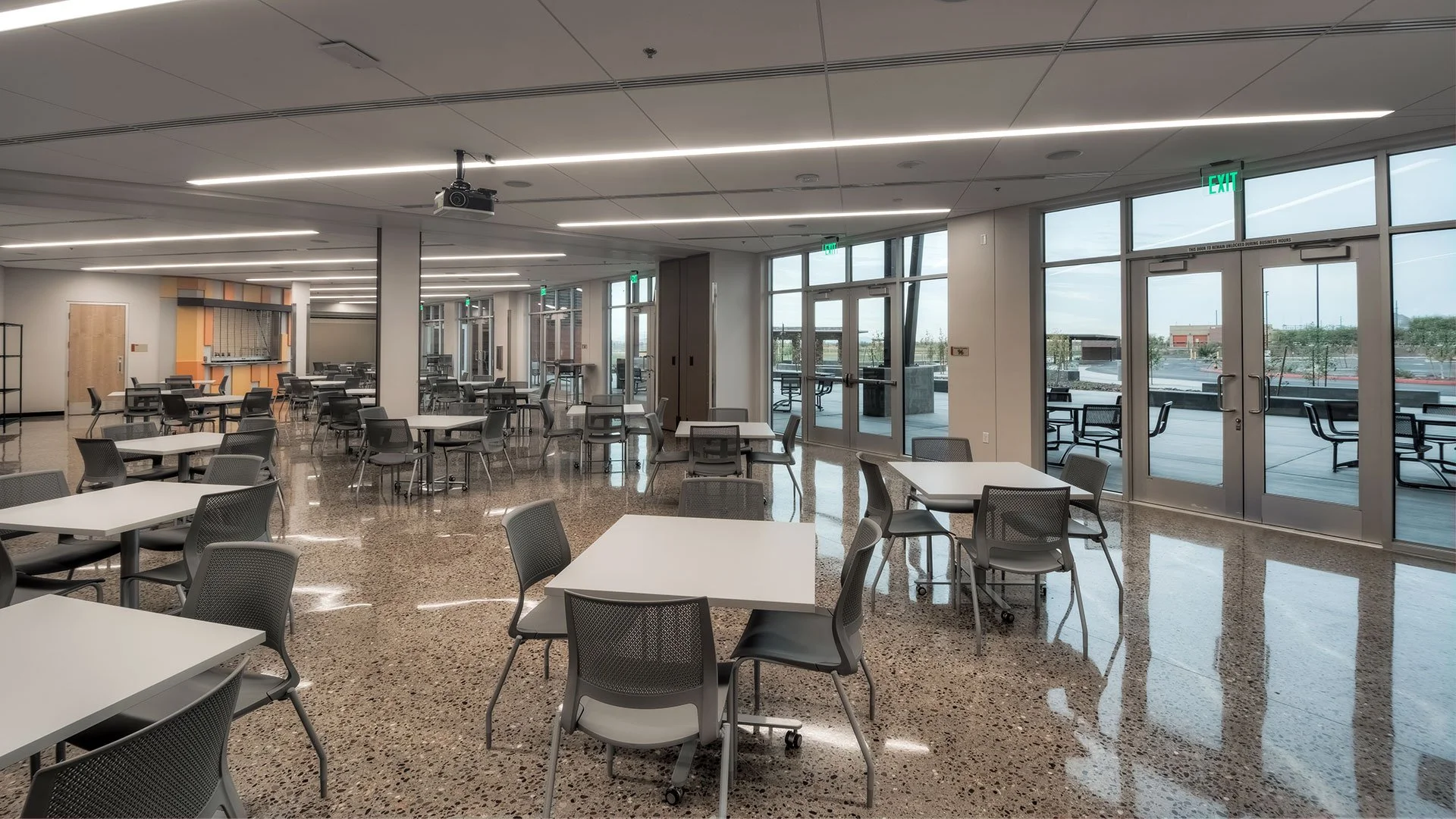 Empty modern cafeteria with white tables and black chairs, large windows, and a polished terrazzo floor.