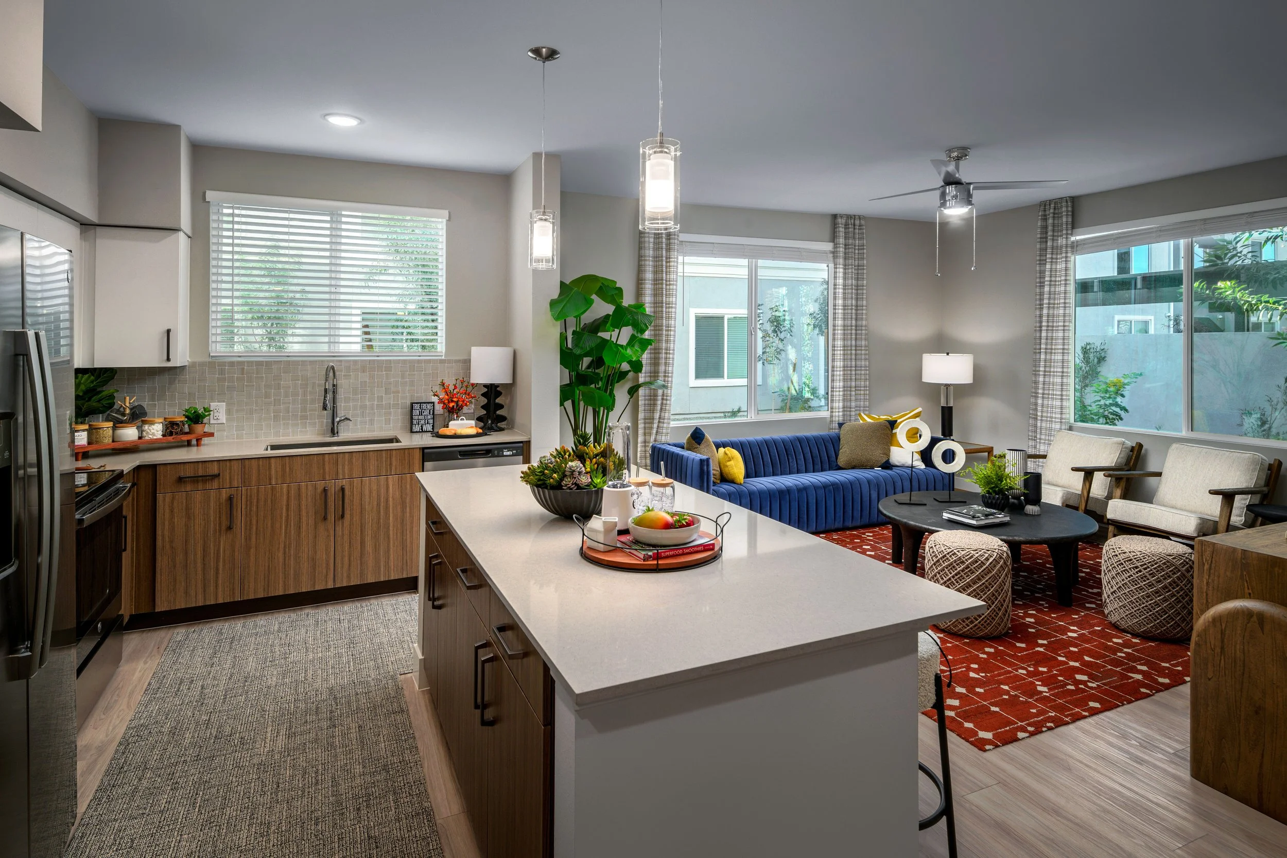 Open living room and kitchen with natural light, modern decor, a blue sofa, a black coffee table, and seating area with armchairs.