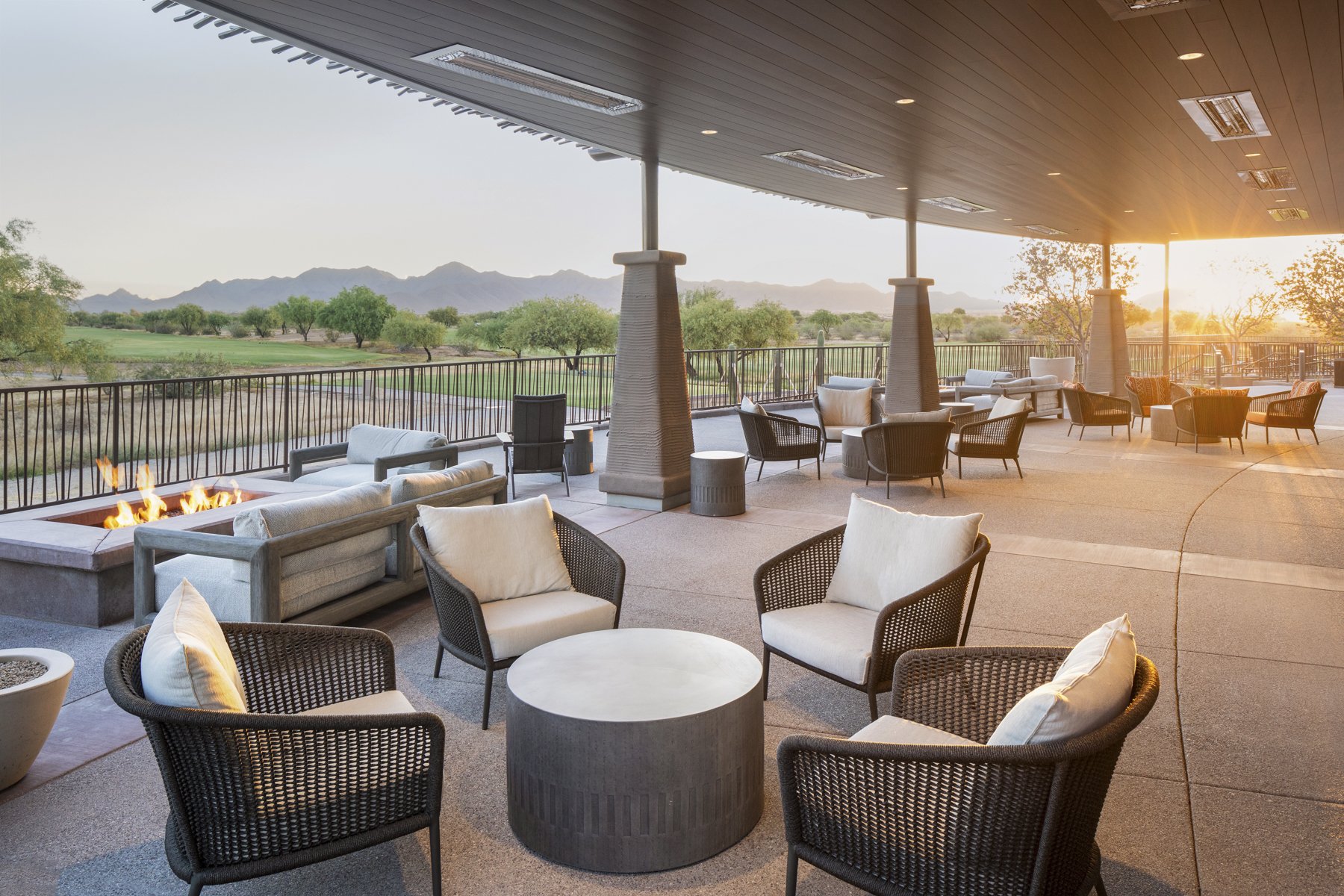 An outdoor patio with modern furniture, a fire pit, and a scenic view of mountains and desert landscape at sunset.