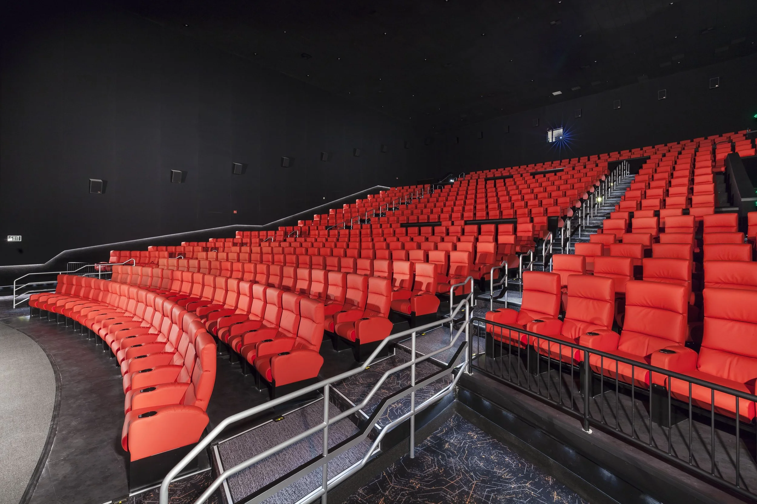 Empty theater with red cushioned seats and black walls, viewed from the stage area.