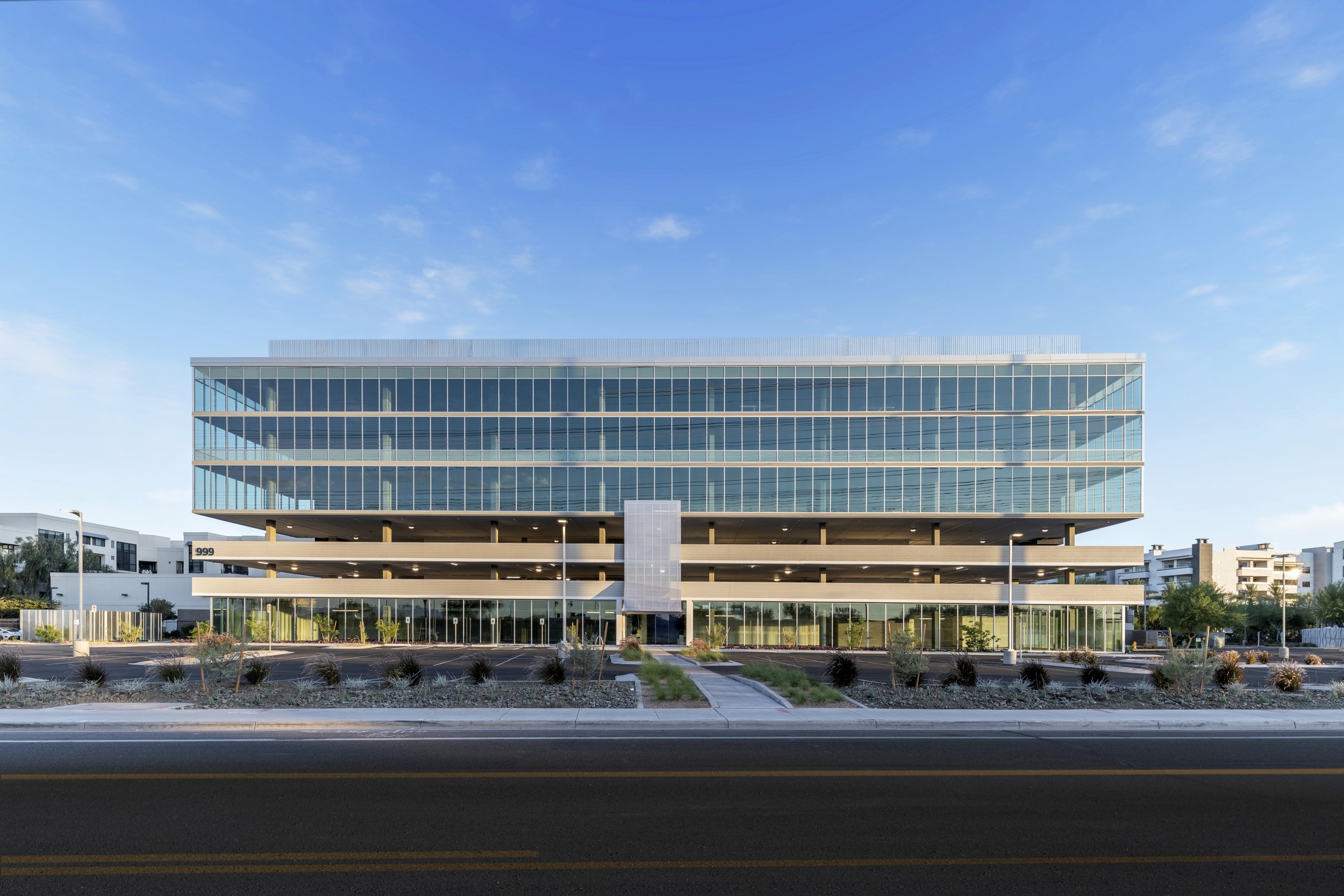 Modern multi-story glass office building with parking garage in front, under a clear blue sky.
