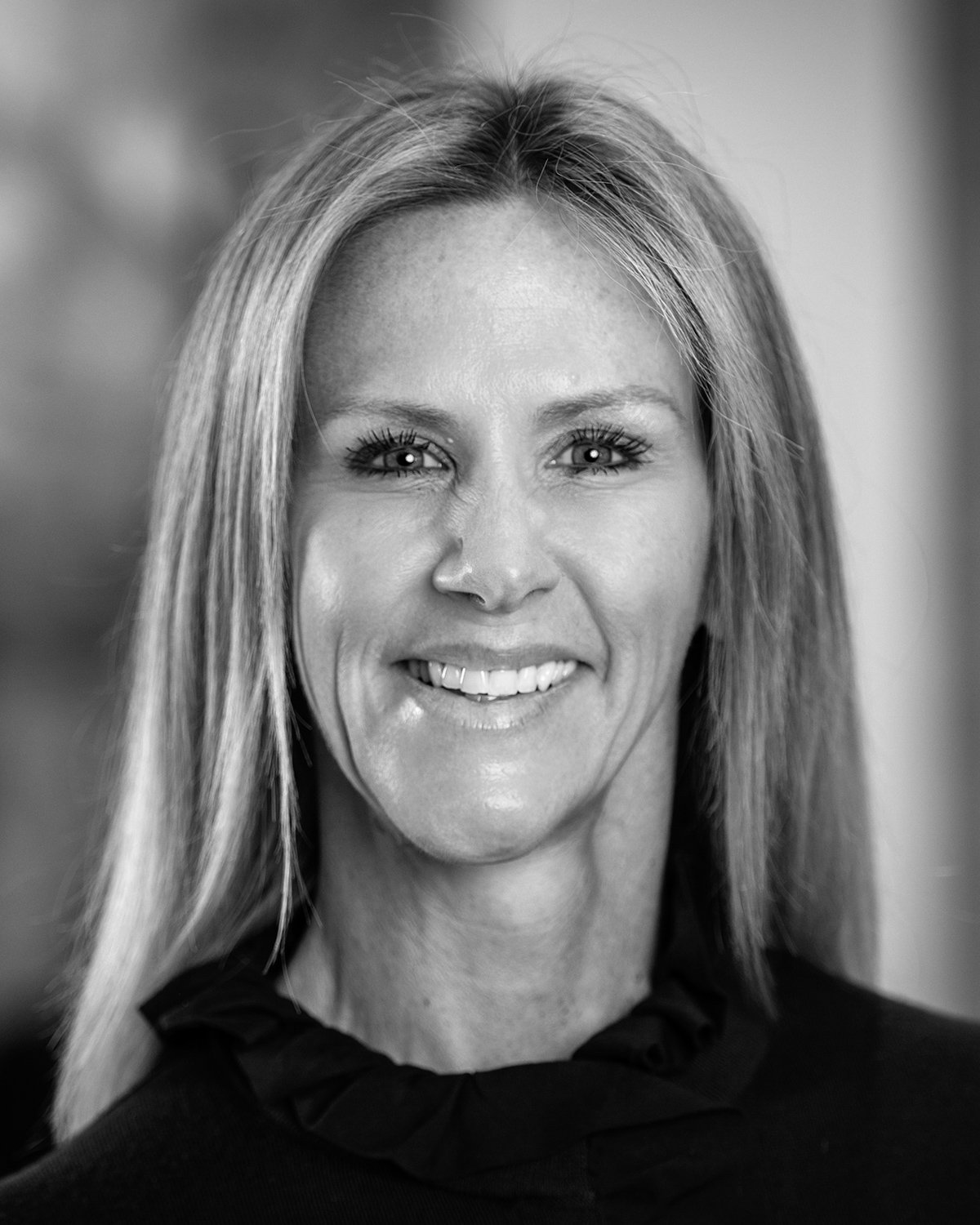 Black and white portrait Melinda Webster, Vice President Business Development and Design at A.R. Mays Construction, smiling, wearing a dark top with a ruffled collar.