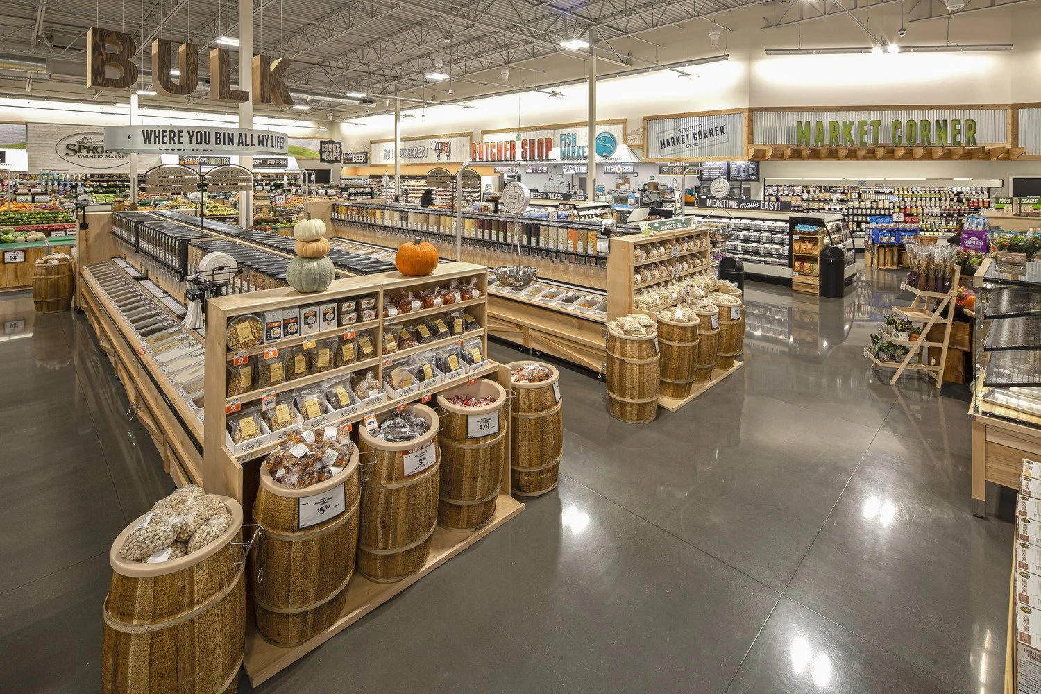 Interior of a grocery store with various sections including bulk items, meats, cheeses, and produce, decorated with pumpkins and fall-themed decor.