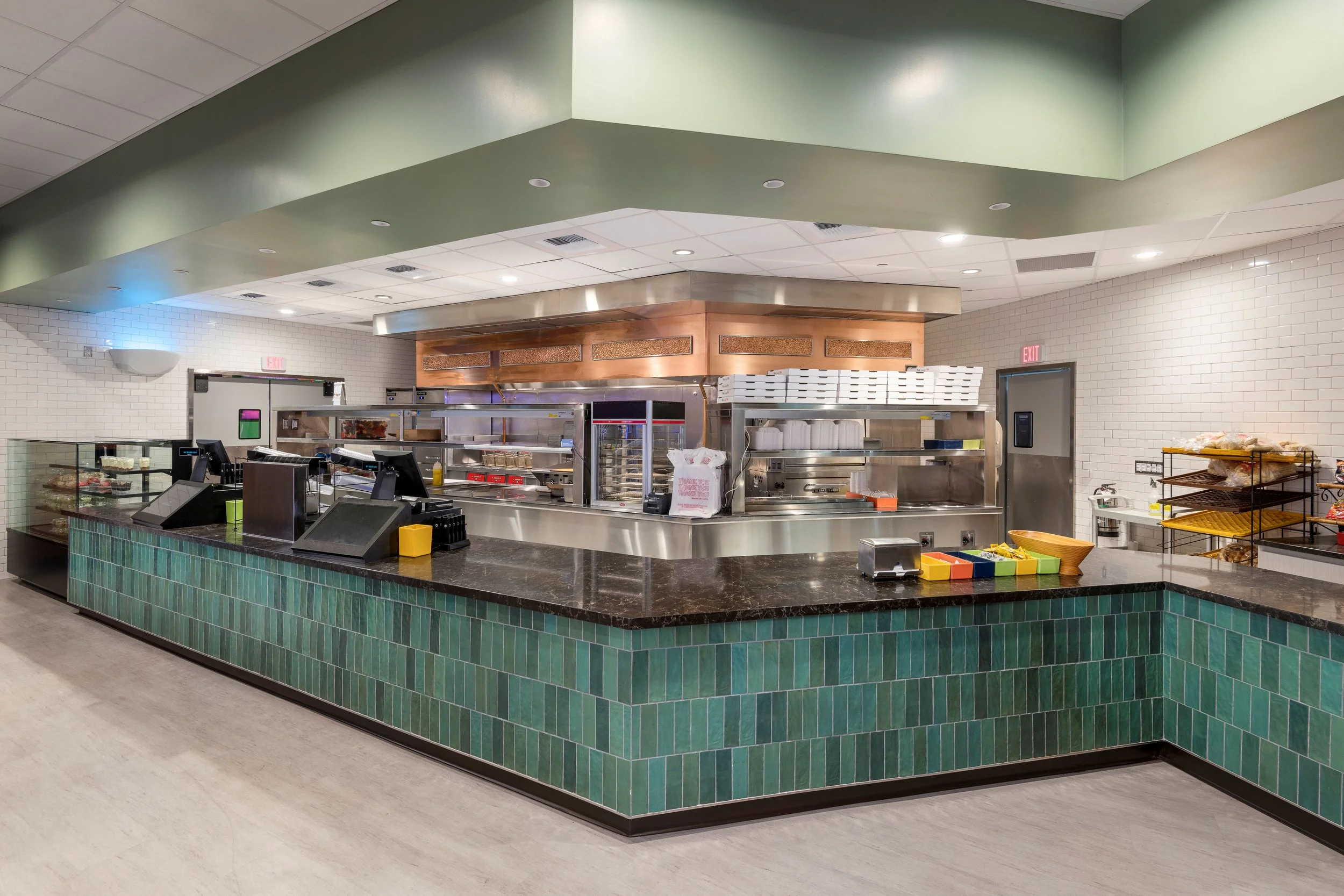 Empty restaurant counter with kitchen behind, green tiled front, some display cases and shelves with food and supplies.
