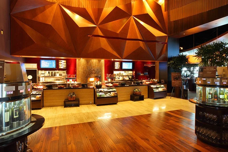Inside a modern restaurant or cafe with a buffet or display counter, illuminated screens, wooden decor, and plants for a warm atmosphere.