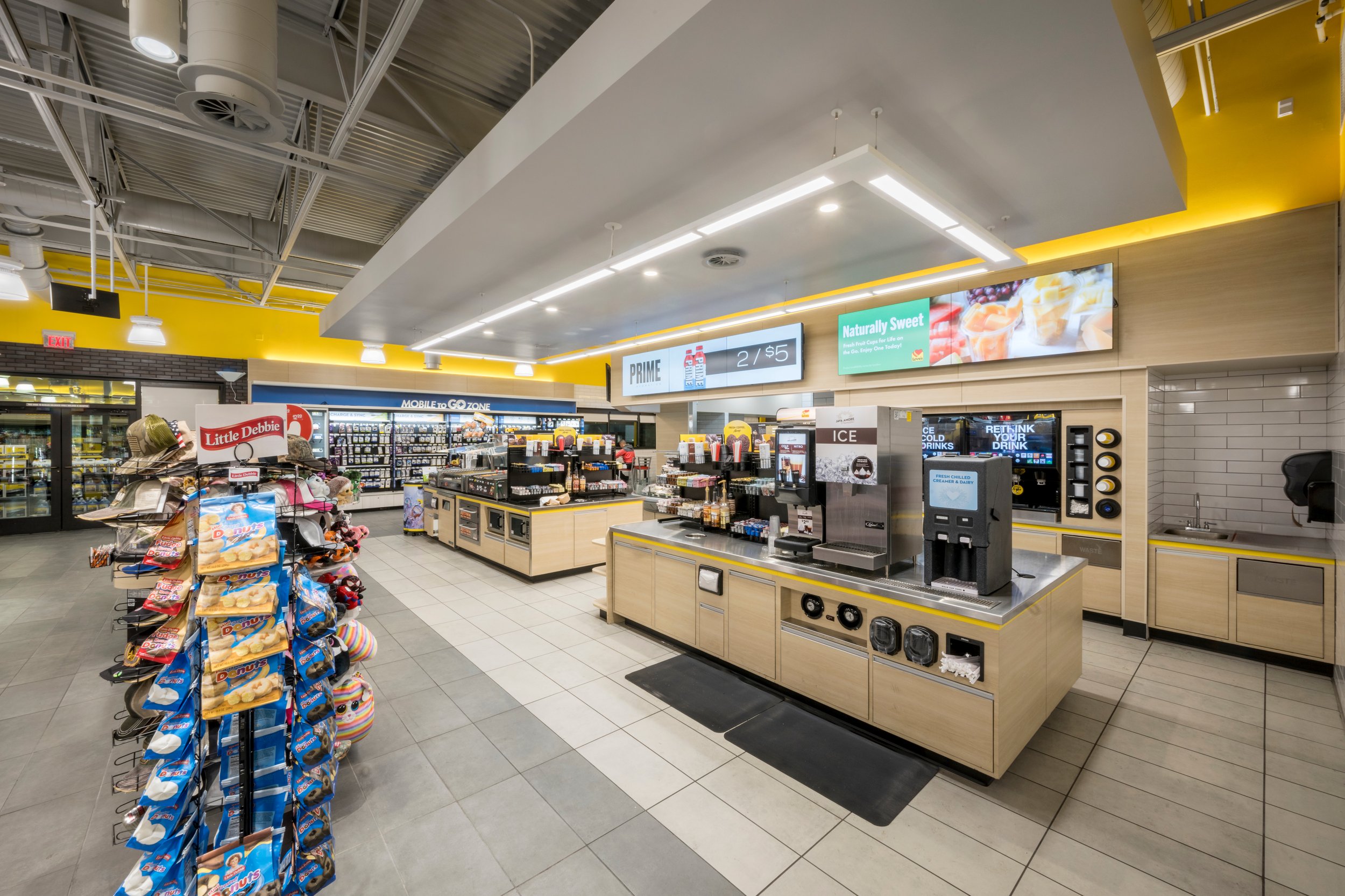 Interior of a grocery store checkout area with snack display, self-serve coffee station, and digital menu boards