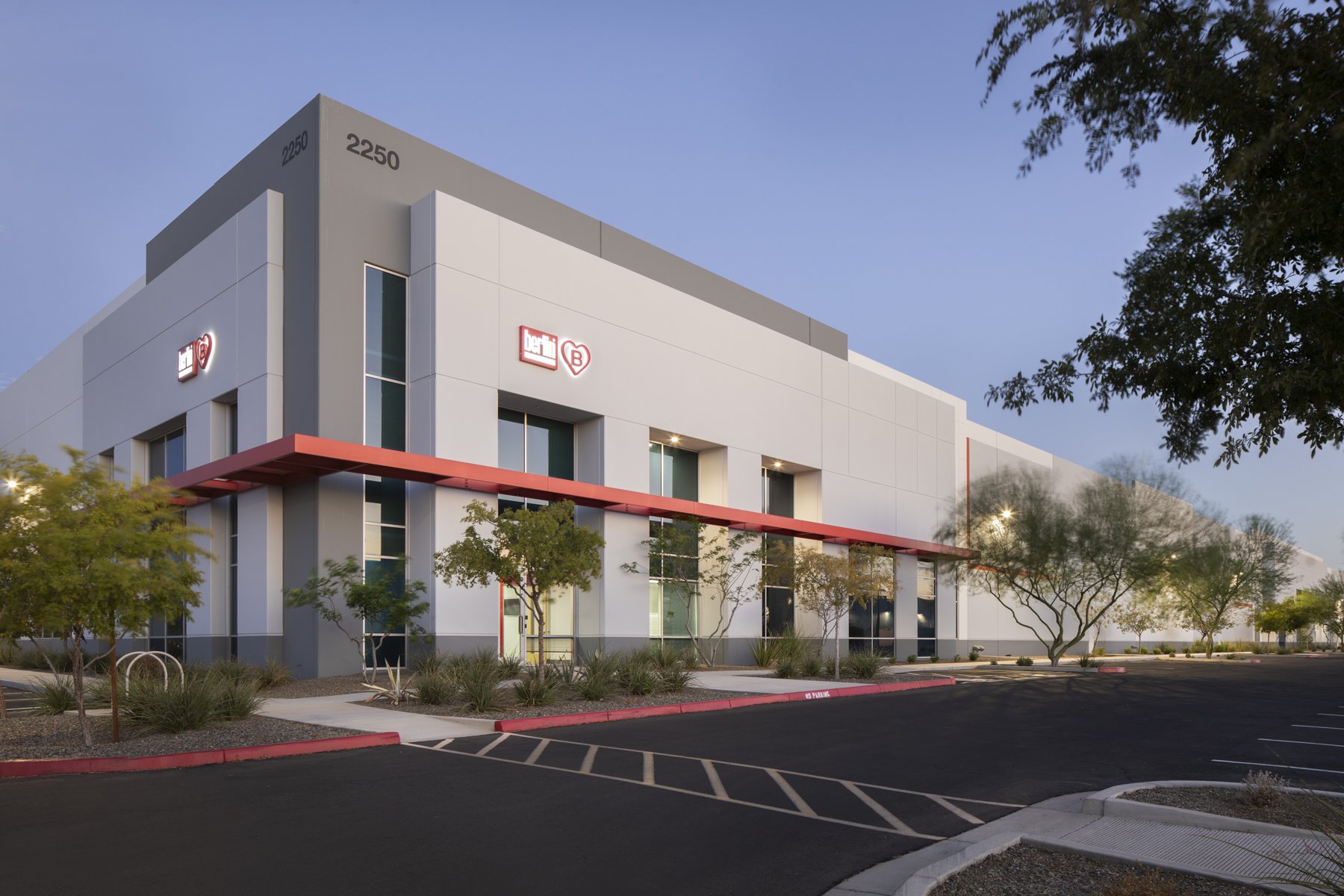 Modern commercial building with signage, trees, and paved parking lot during early evening.