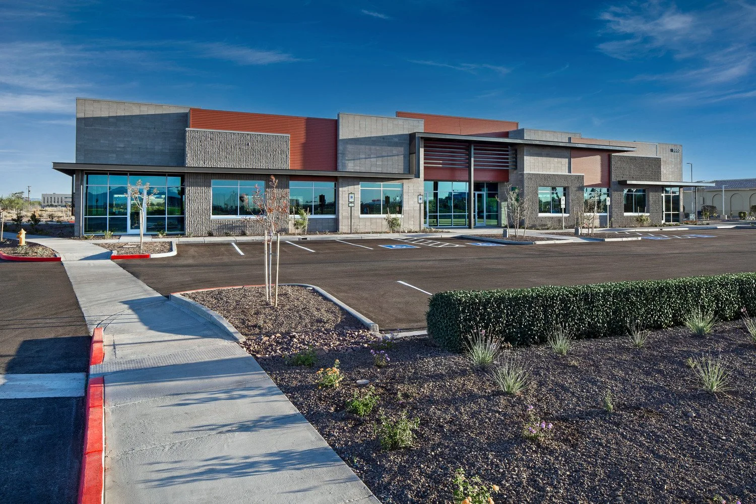 Modern commercial building with large glass windows, trees, and a parking lot in front, under a partly cloudy sky.