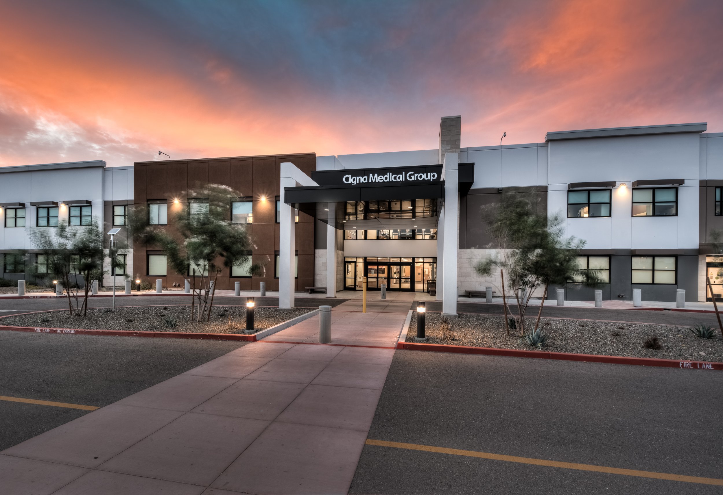 Exterior view of Cigna Medical Group building during sunset with a colorful sky, pathway leading to the entrance, and small landscaping plants.