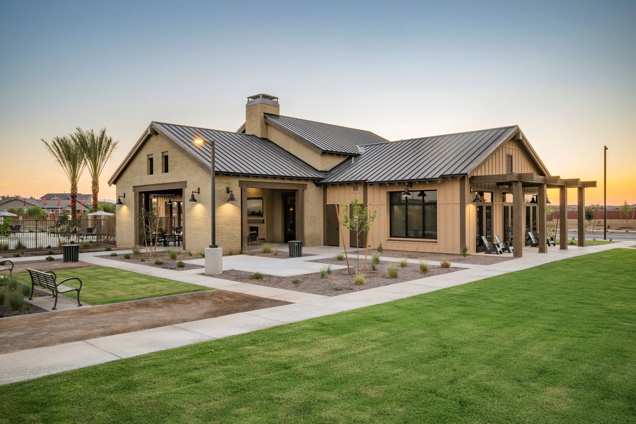 A modern residential building with a metal roof, surrounded by a well-maintained lawn, walkways, and outdoor seating area at sunset.