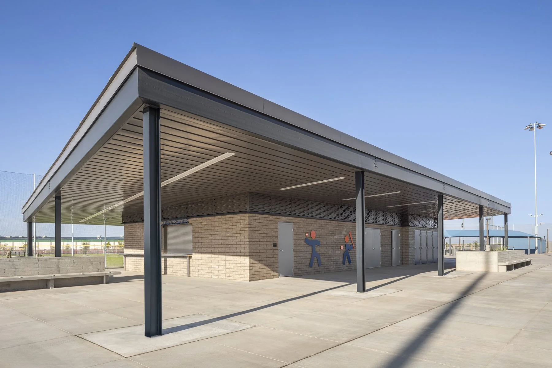 Empty outdoor sports facility building with a metal roof, brick walls, and cartoon basketball player murals on the wall, with a clear blue sky in the background.