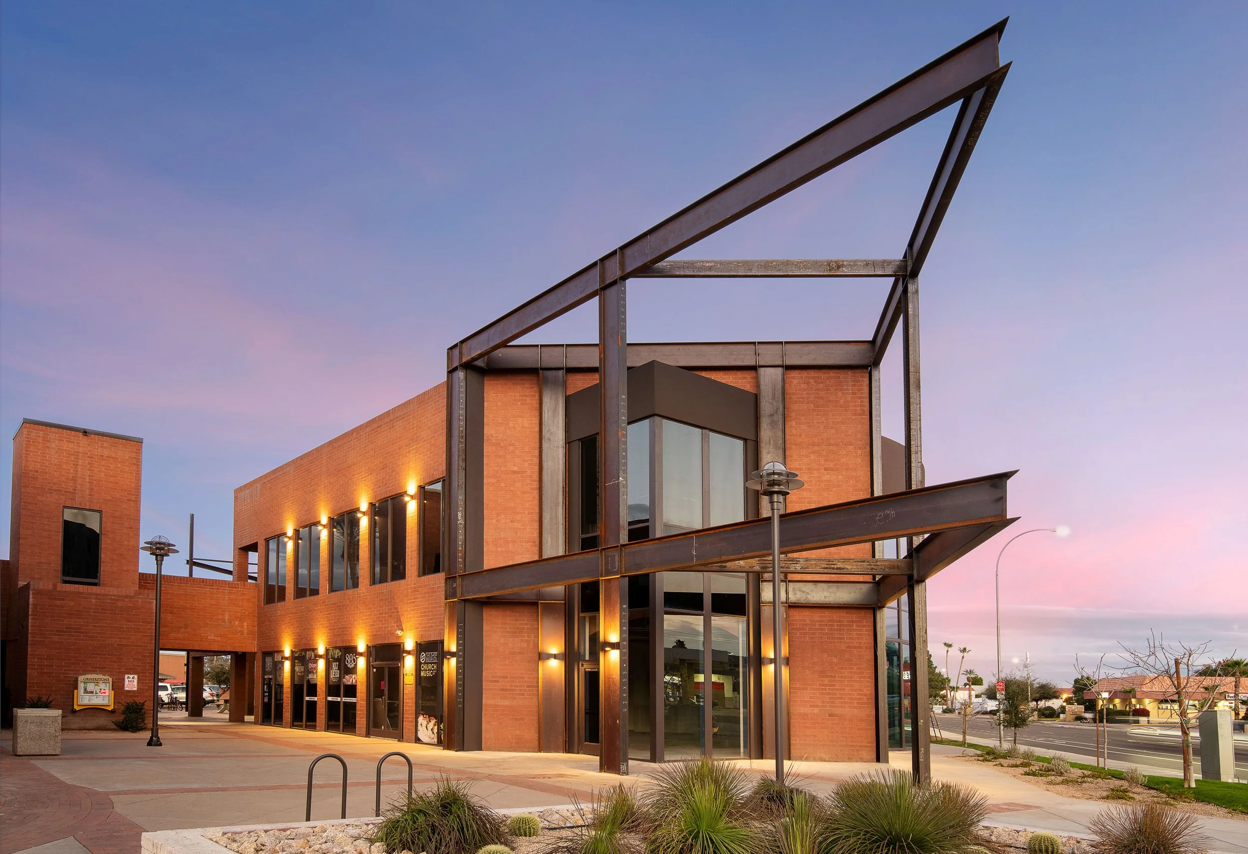 A modern brick building with large glass windows and steel framework during dusk with a pink and purple sky.
