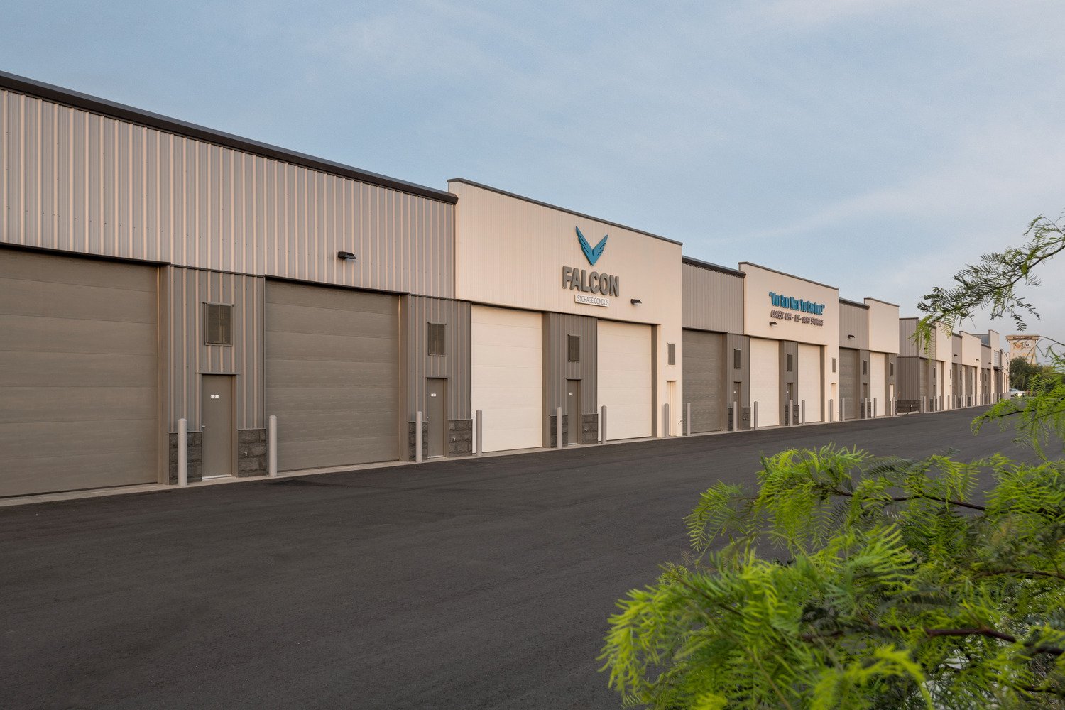 Exterior view of a storage facility named Falcon Storage Condos with multiple garage units, signage, and a paved driveway, with some greenery in the foreground.