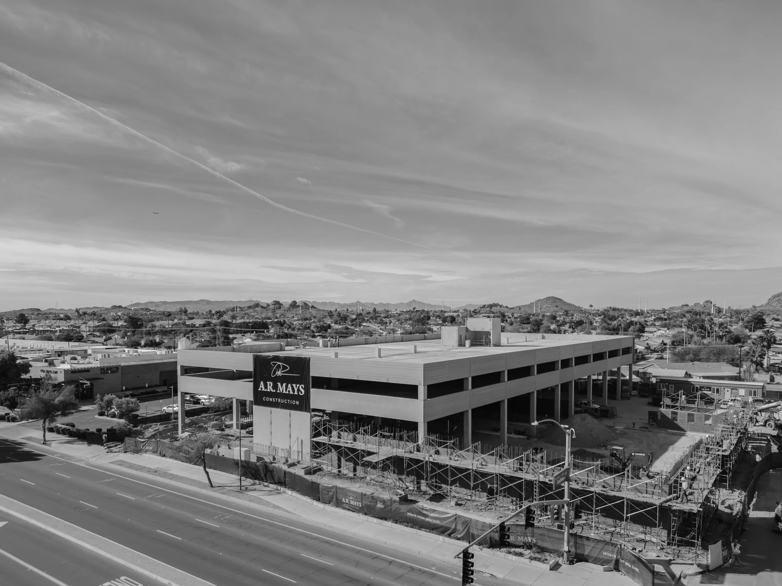 Construction site of a multi-story parking garage with a 'A.R. Mays Construction' sign and scaffolding and equipment, along a busy road with streetlight and traffic signal.