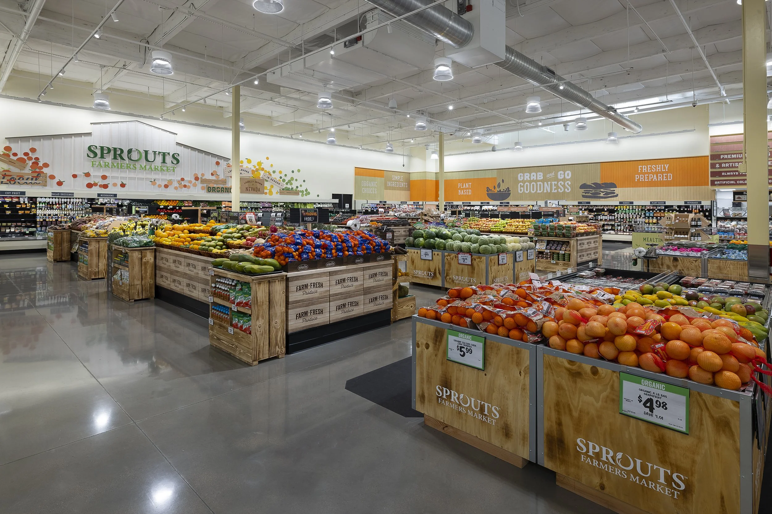 Interior of a grocery store's produce section with various fruits and vegetables displayed in wooden crates and baskets, with signage indicating organic and farm-fresh products.