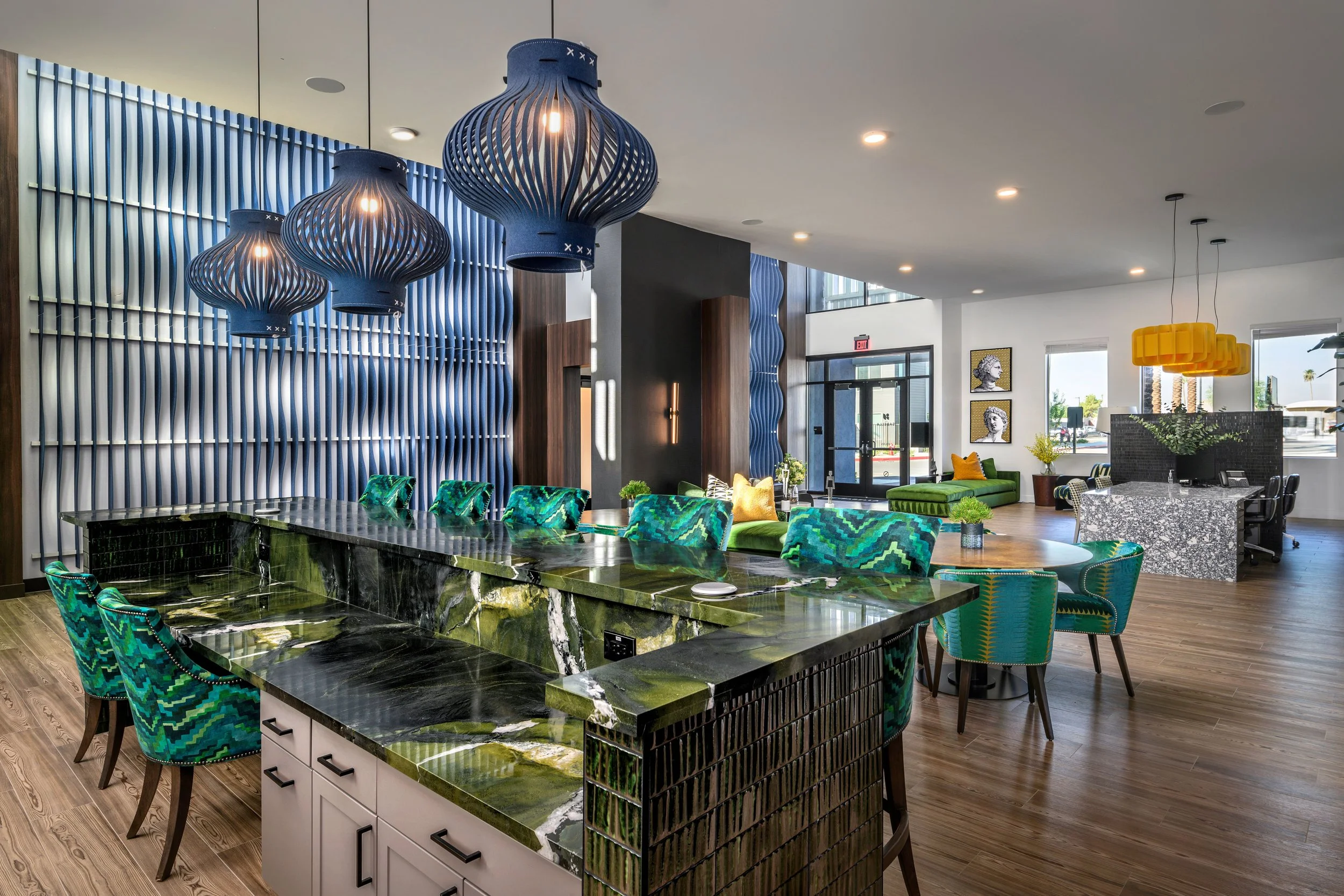 Modern interior with a large green marble kitchen island, colorful patterned chairs, blue pendant lights, and contemporary decor.