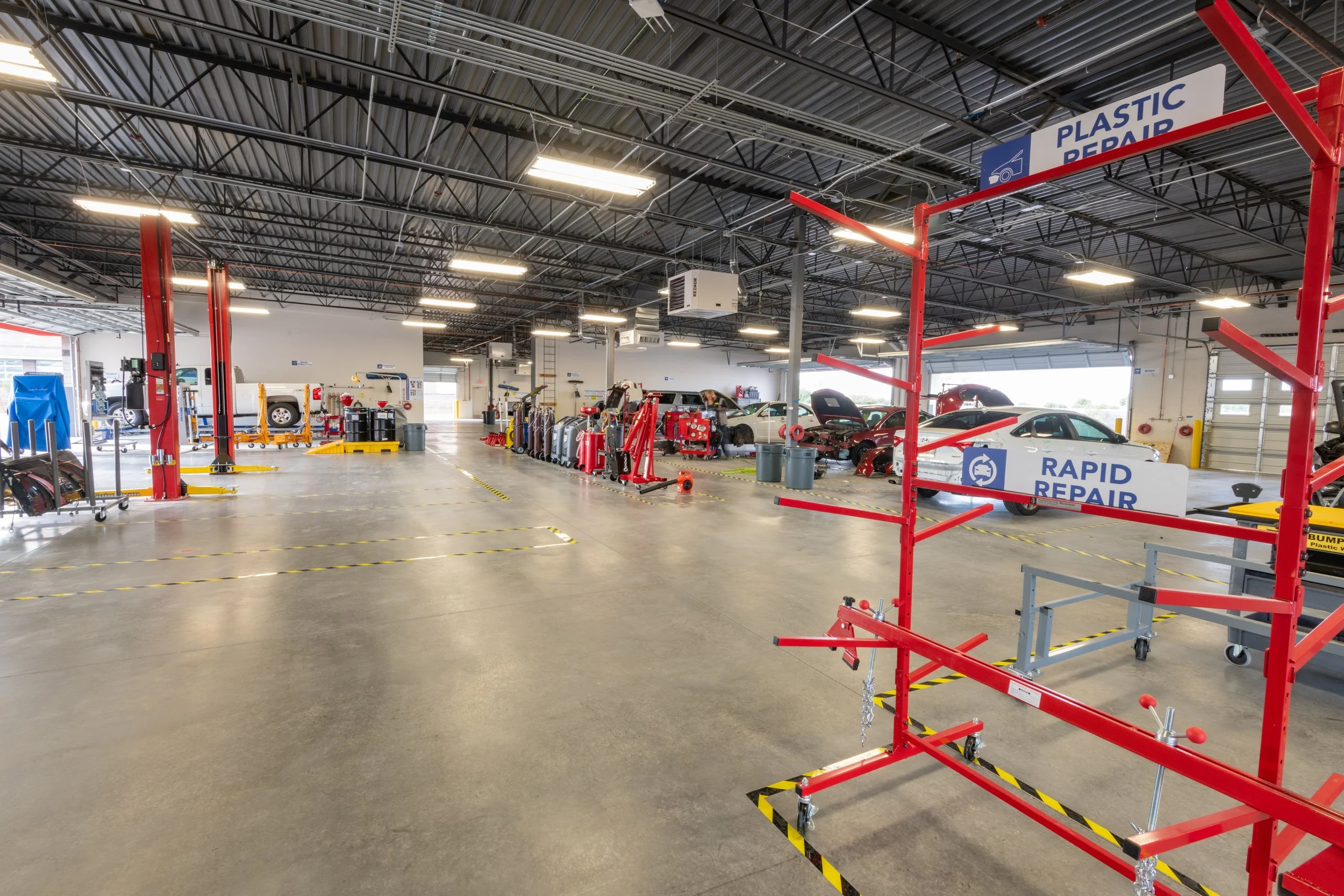 Automotive repair shop with cars on lifts, tools, and signage for plastic repair and rapid repair services.