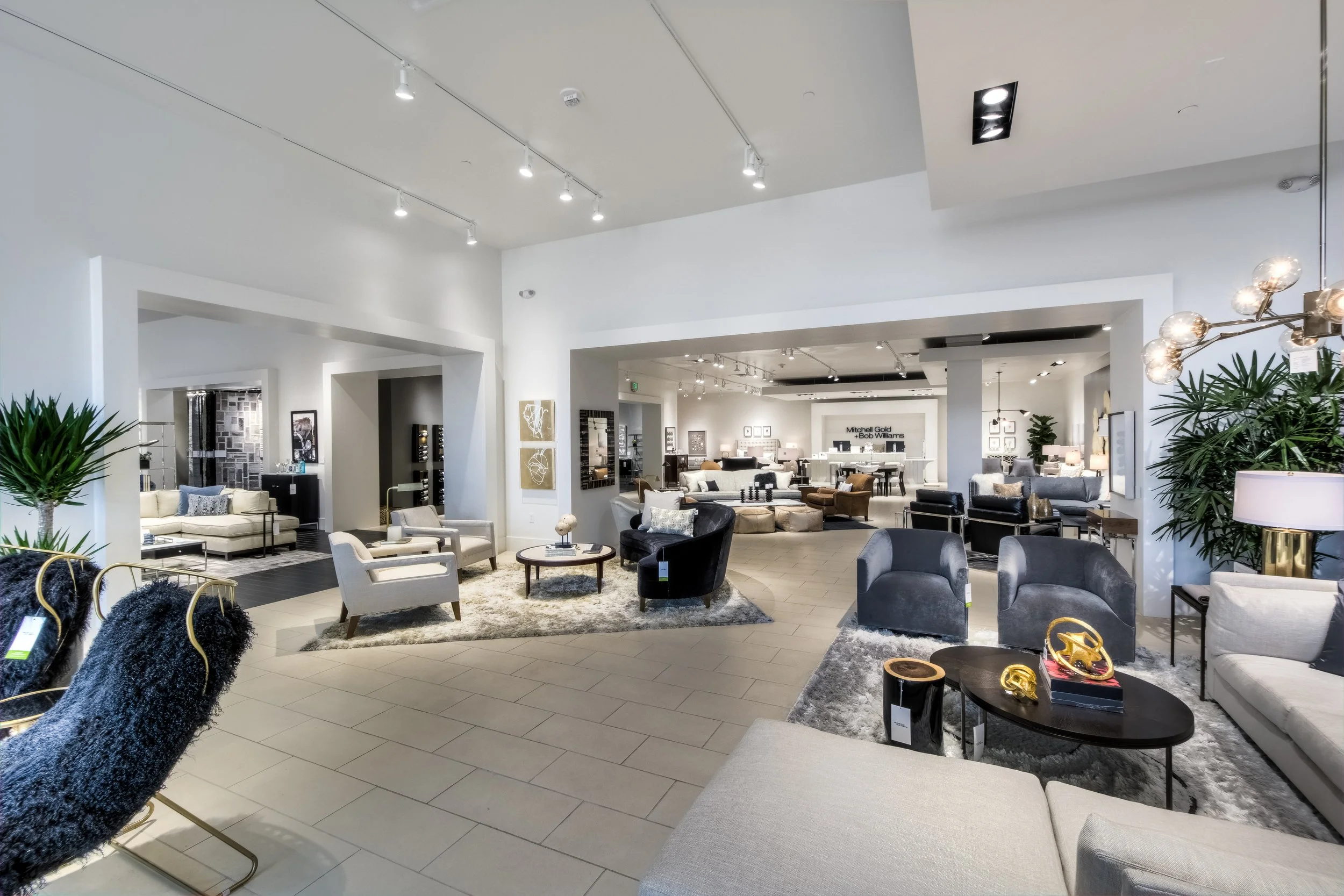 A spacious furniture showroom displaying various sofas, chairs, and coffee tables arranged in a modern, well-lit setting.