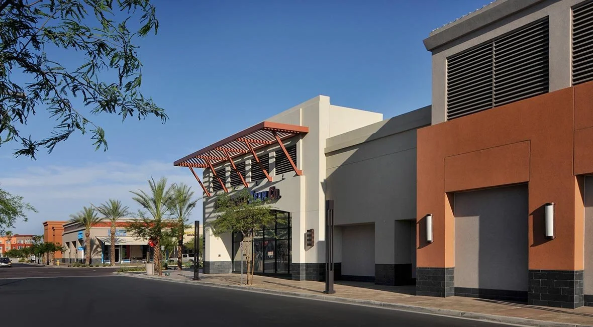 Empty shopping plaza with retail stores, palm trees, and a clear blue sky.