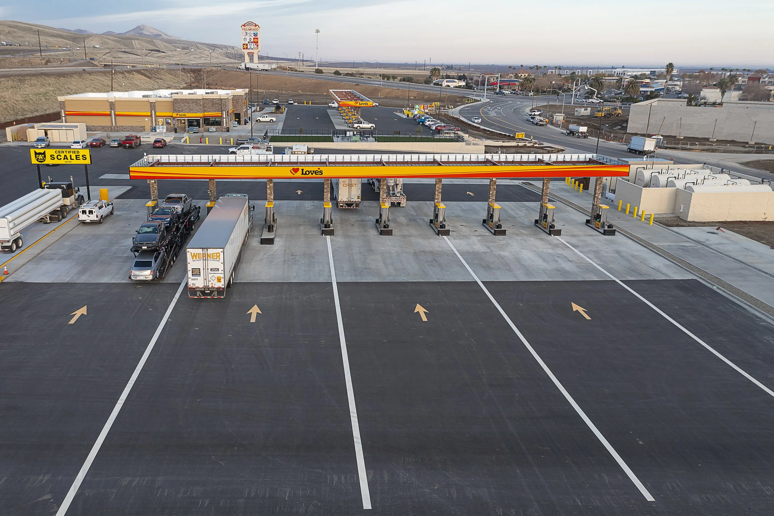 Empty drive-thru lanes at a parking lot with a Love's gas station and convenience store in the background, situated in a semi-arid area with mountains in the distance.