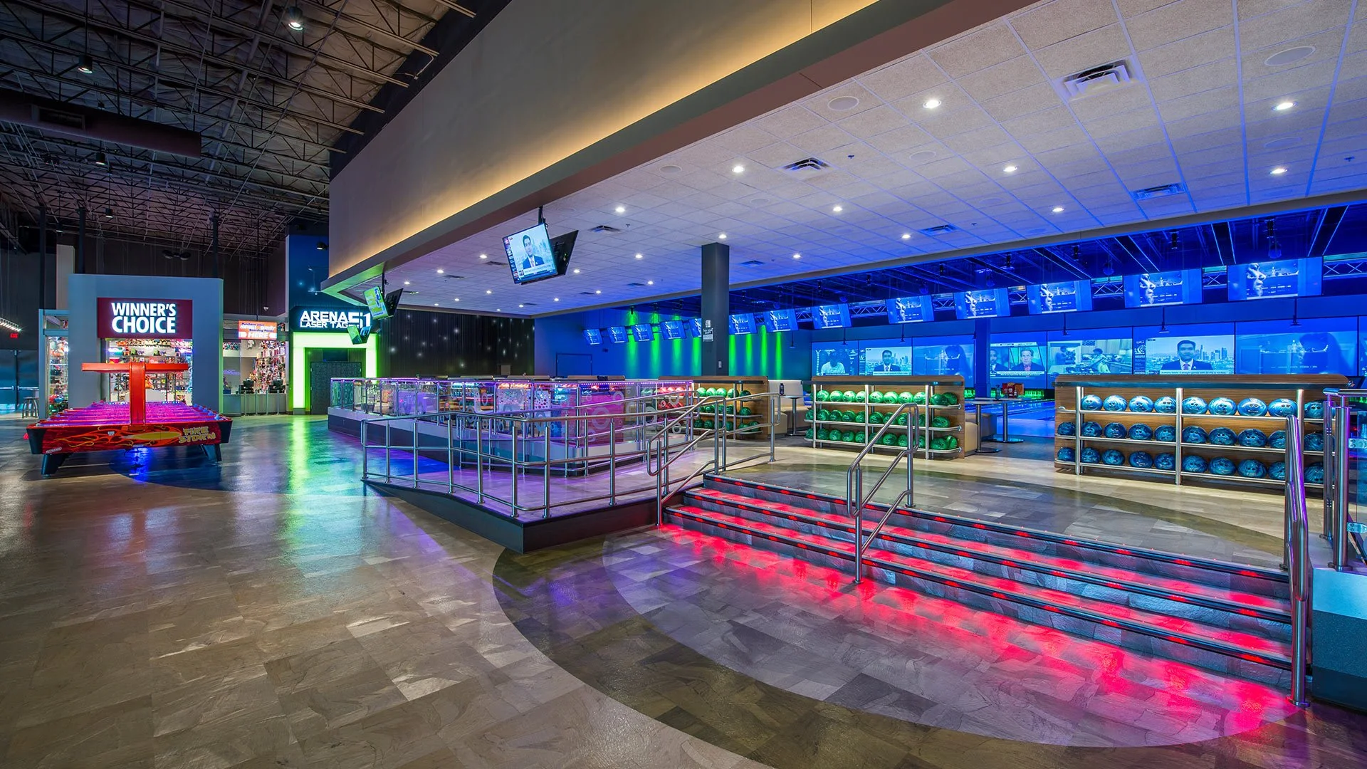 Empty indoor entertainment center with bowling lanes, arcade games, laser tag, and large screens, illuminated by colorful LED lights.