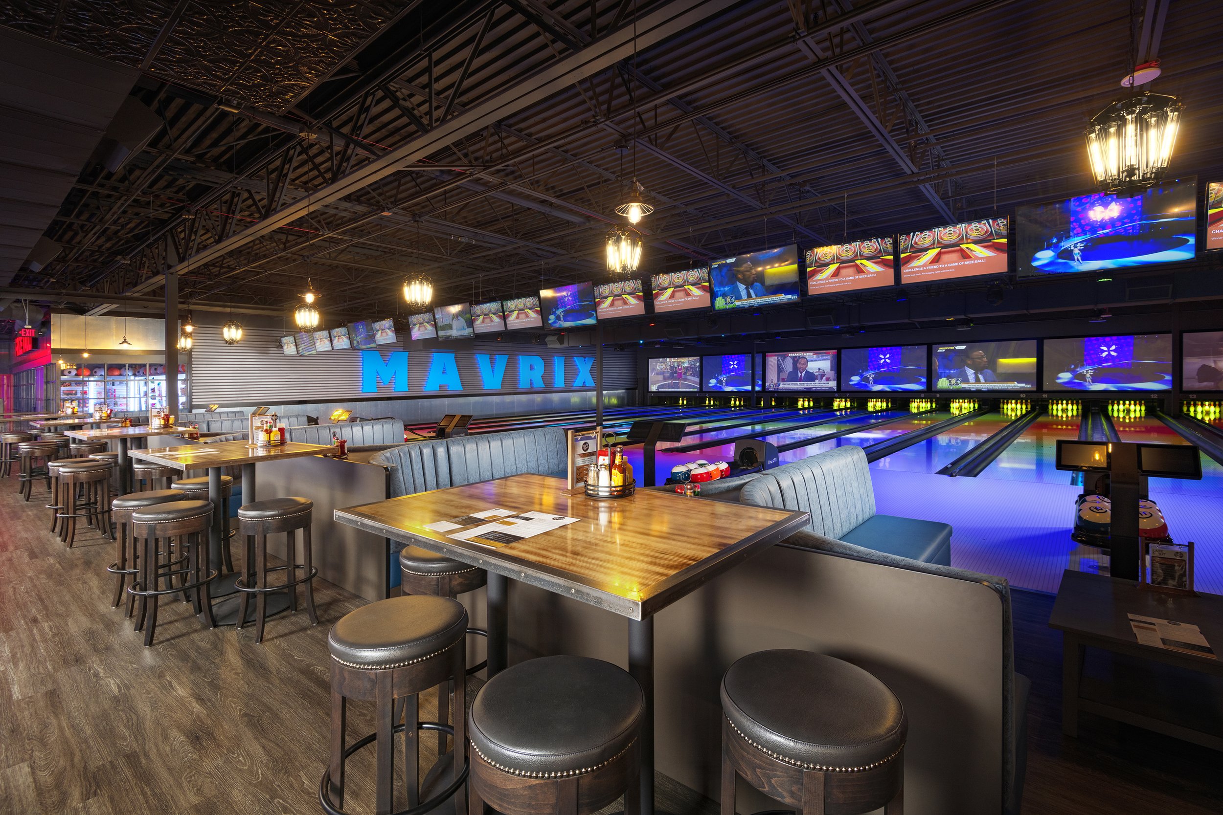 Interior of a modern bowling alley with lanes, seating area, TV screens, and a large blue sign that says 'MAVRIX'.