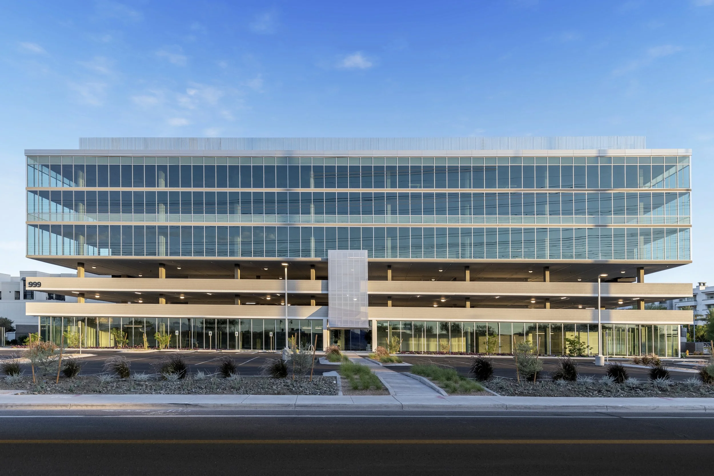 Modern multi-story office building with glass facade and parking area in front.