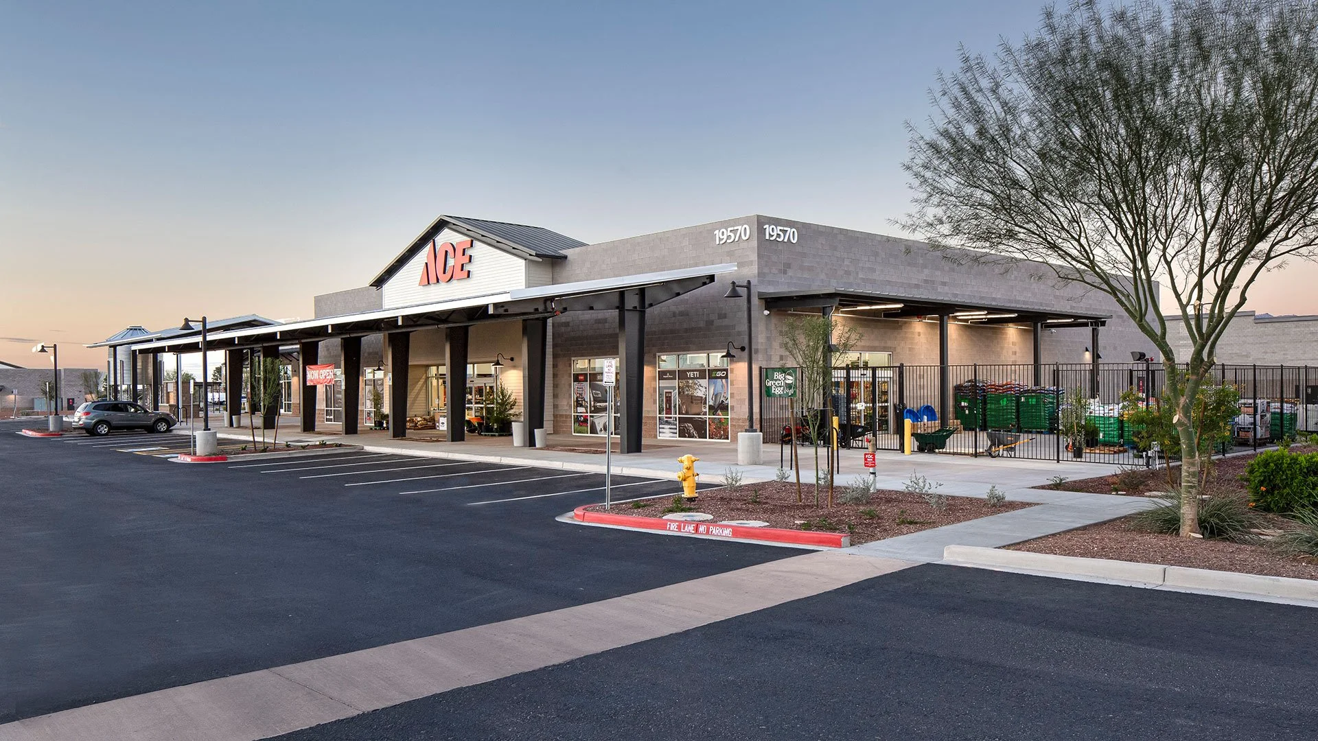 Exterior view of an ACE hardware store with parking lot in front and some shopping carts near the entrance during early evening.