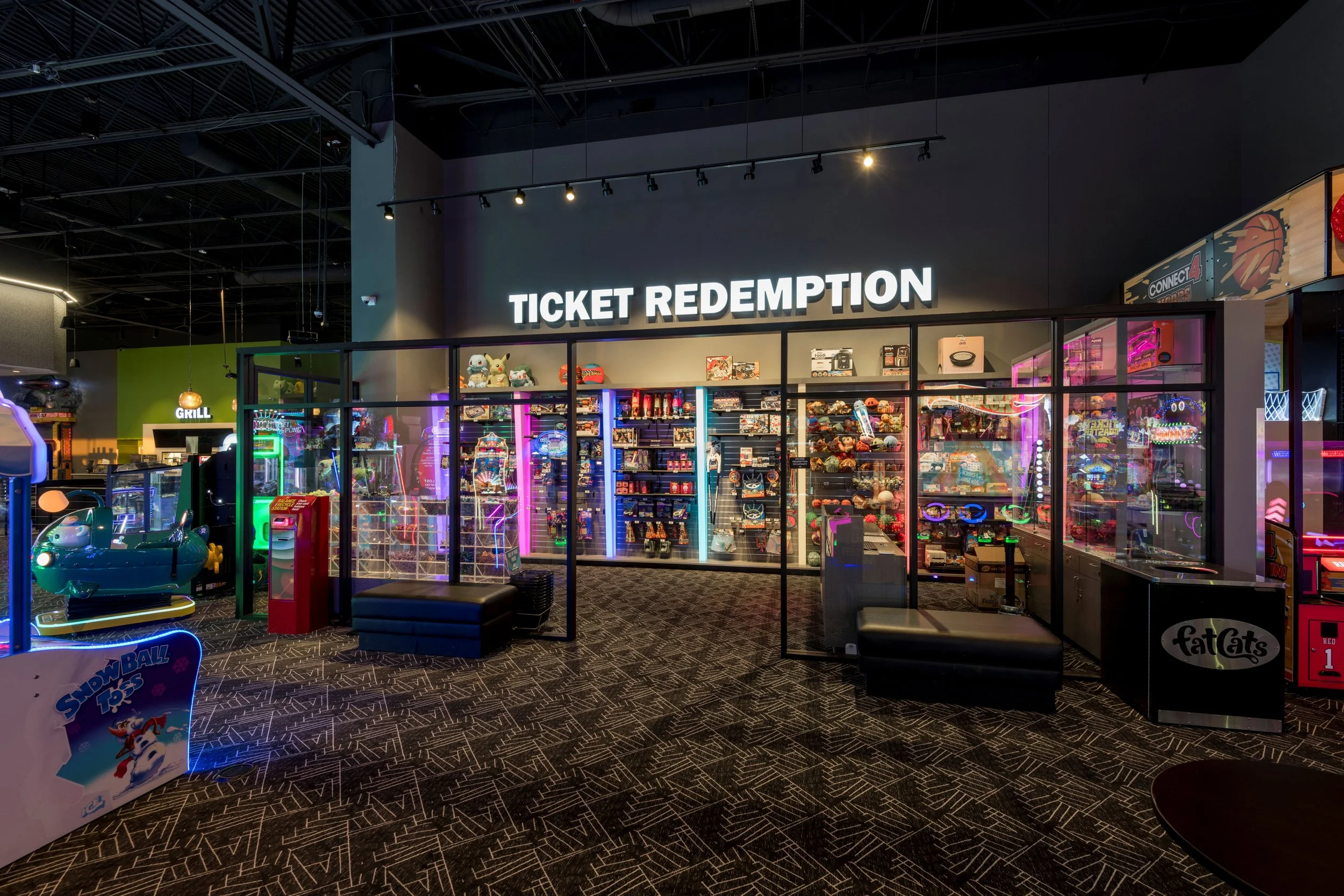 Arcade game redemption area with various video games and prizes, illuminated by colorful neon lights.