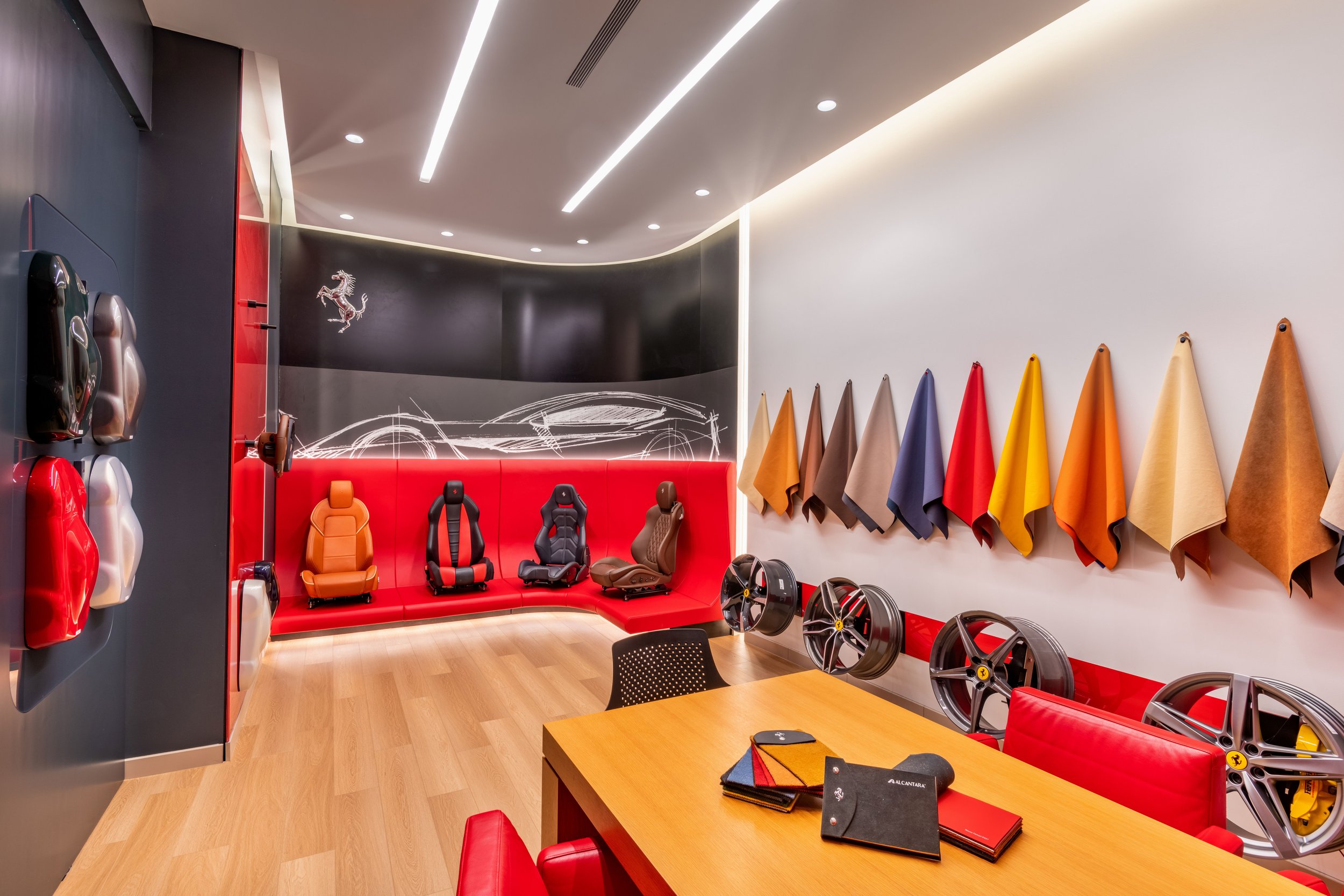 Showroom with Ferrari-themed decor, car seat samples, fabric swatches, and car wheels display.