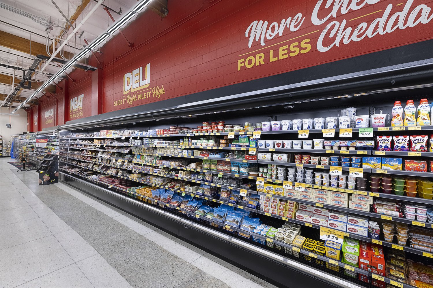 Supermarket aisle with dairy products including yogurt, butter, and cheese on shelves under red signage.