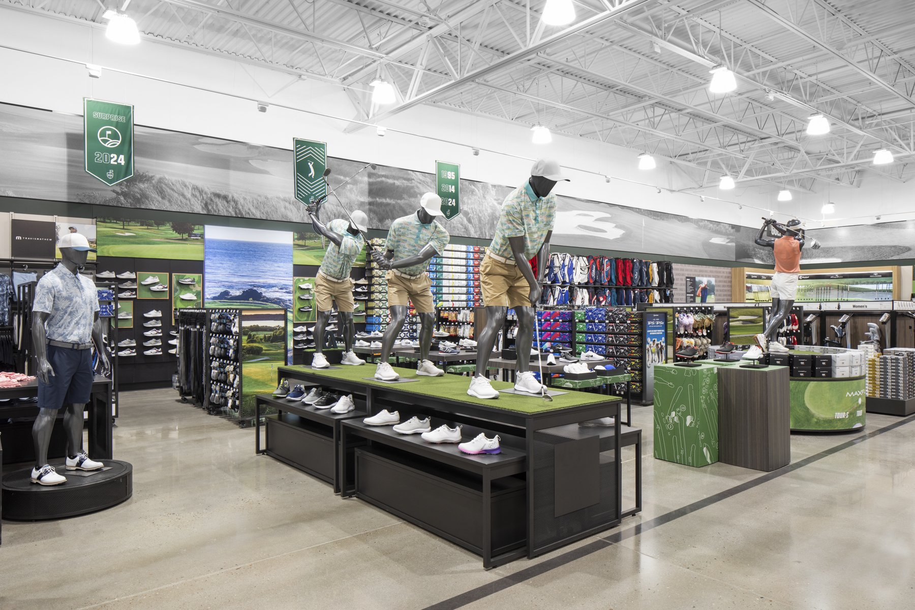 Mannequins dressed in golf attire holding golf clubs inside a golf equipment store.