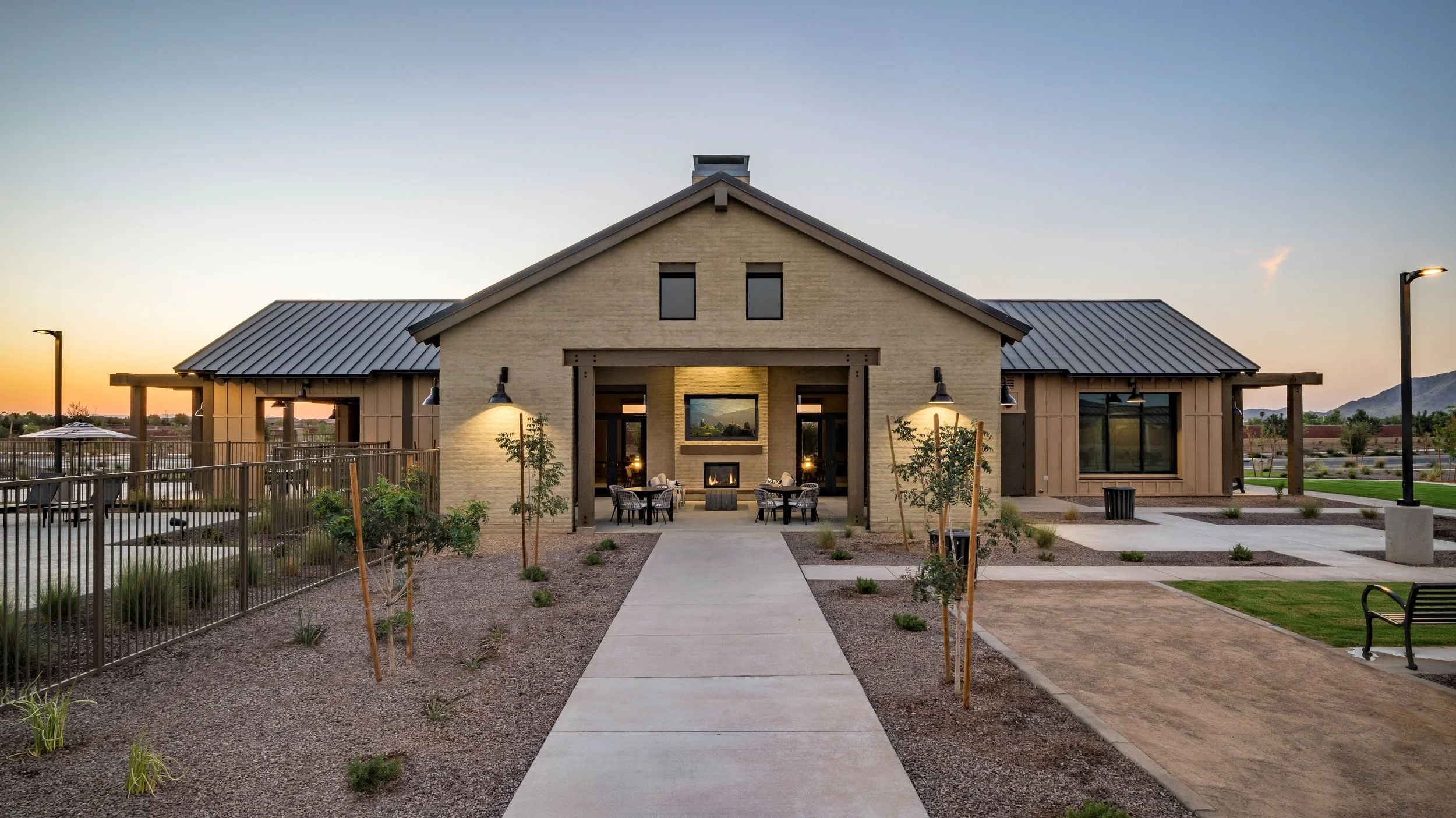 Modern building with a gravel and paved outdoor area, outdoor seating, and landscaping, under a sunset sky.