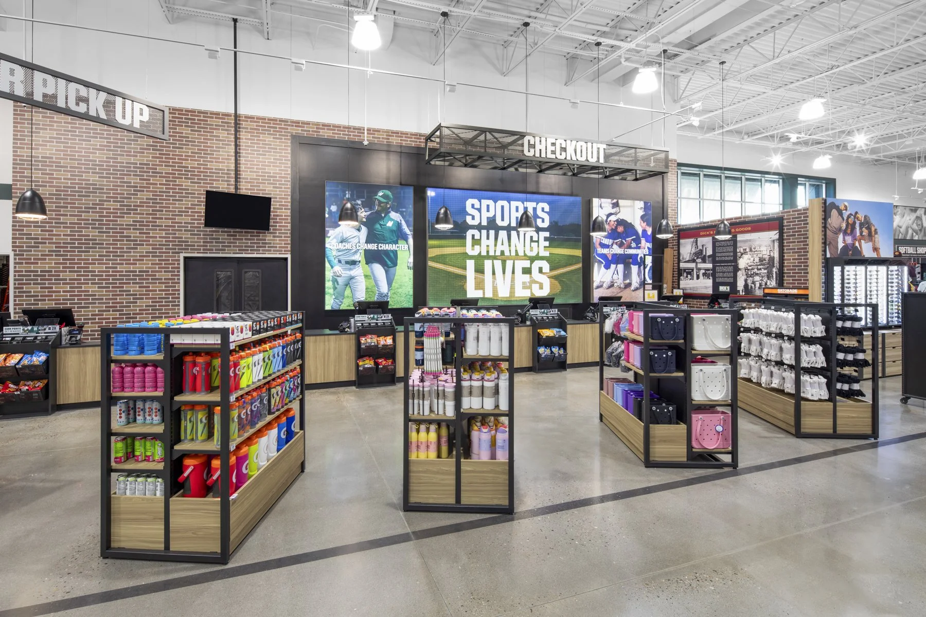 Inside a sports retail store with shelves of athletic merchandise, large digital screens displaying sports images and the message "Sports Change Lives," and checkout counters.