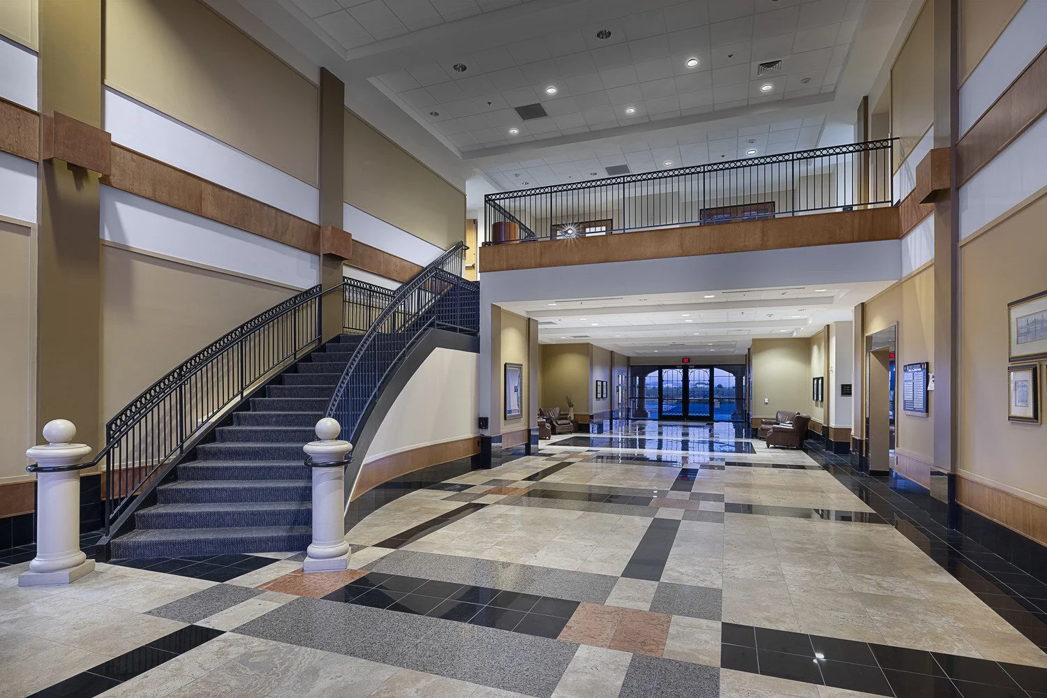 Empty hotel lobby with a staircase, seating area, and glass doors in the background.