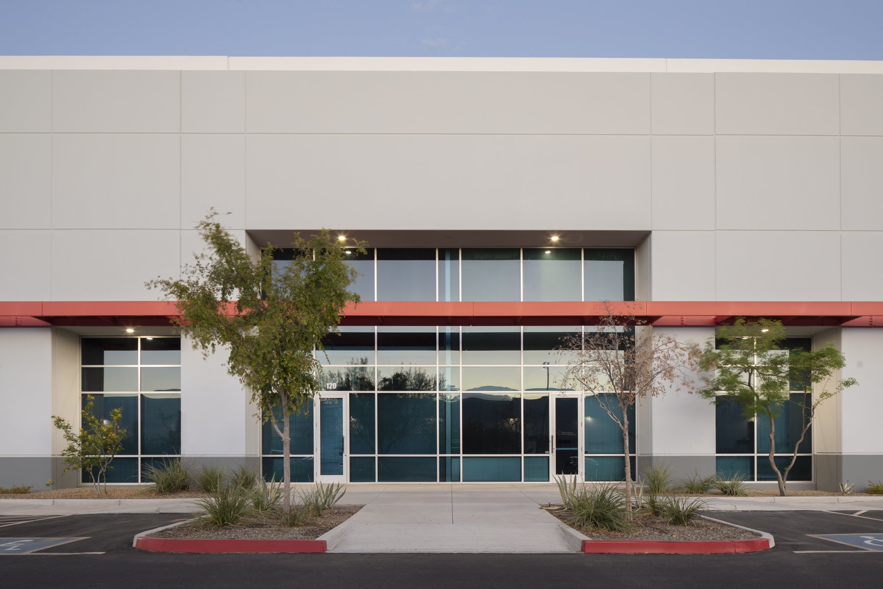 Modern commercial building with large glass windows, trees, and a parking lot in front.