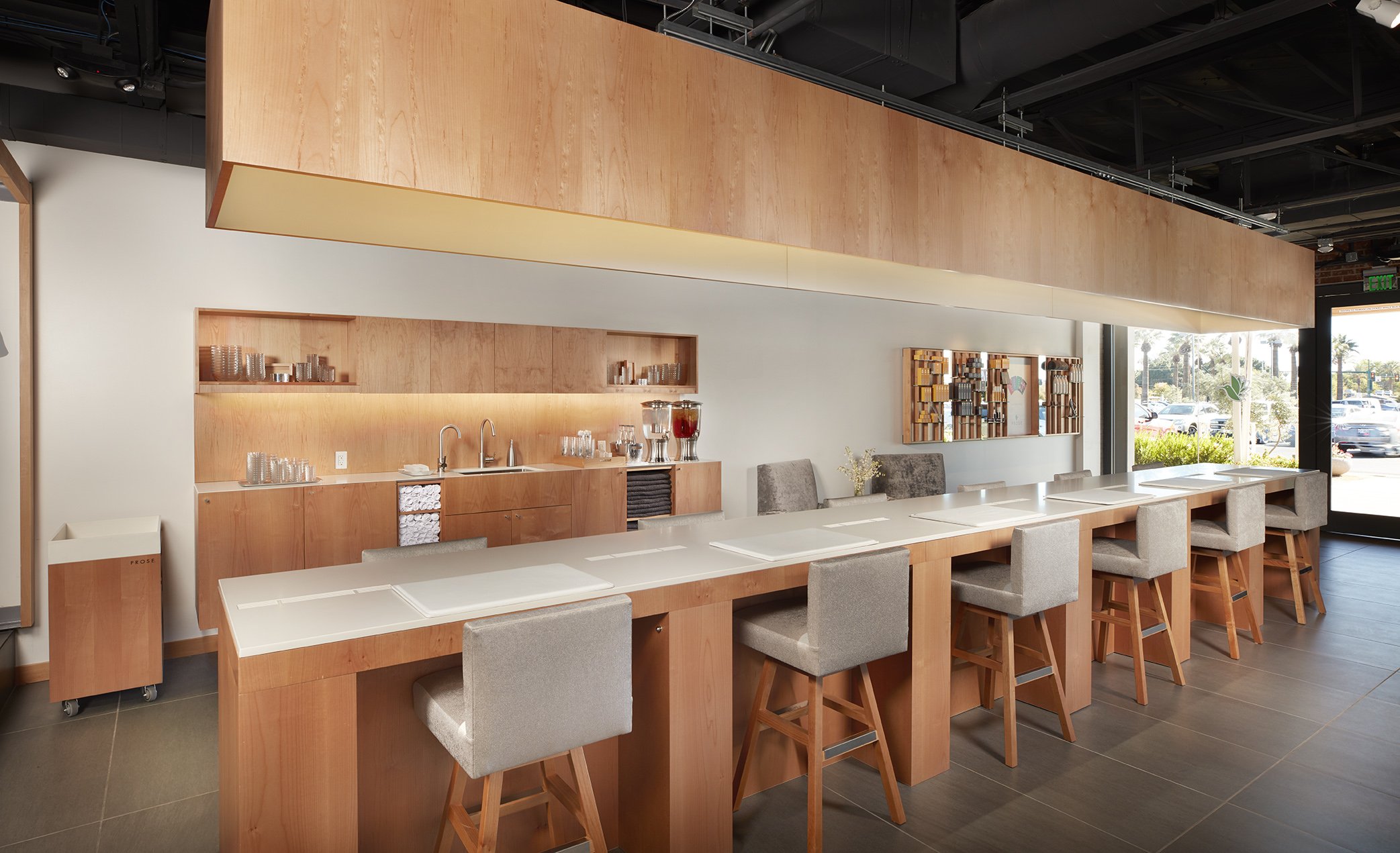 Empty restaurant with a long counter, chairs, and a wood interior, near large windows showing outside parking lot.