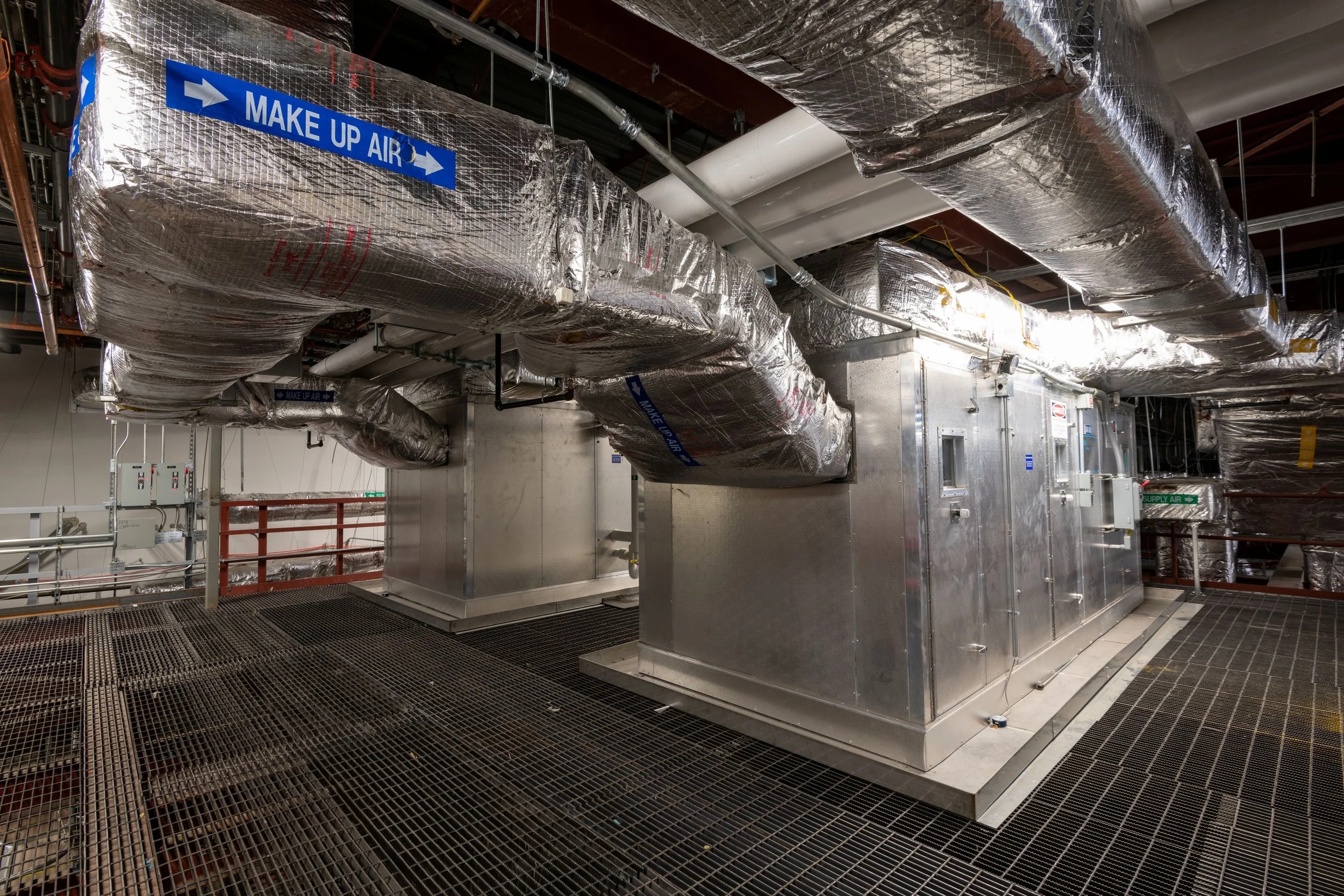 Elevated view of an industrial HVAC system with large insulated ductwork, metal equipment, and signages indicating make-up air and supply air.