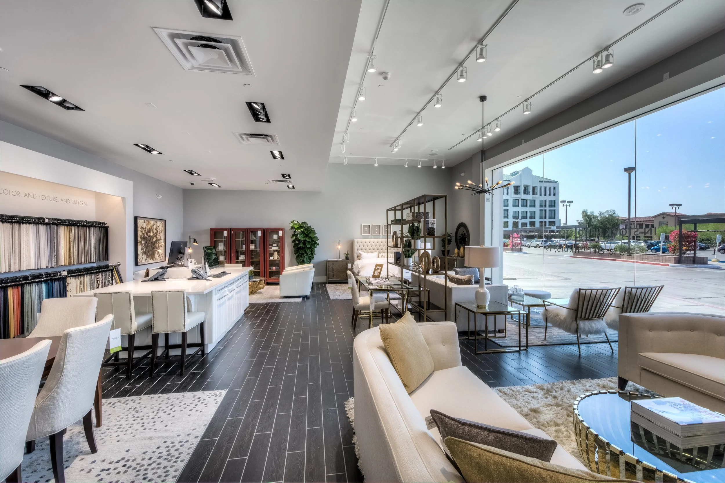Interior of a modern furniture store showcasing sofas, chairs, and decor accents with a glass storefront view of the parking lot and buildings outside.