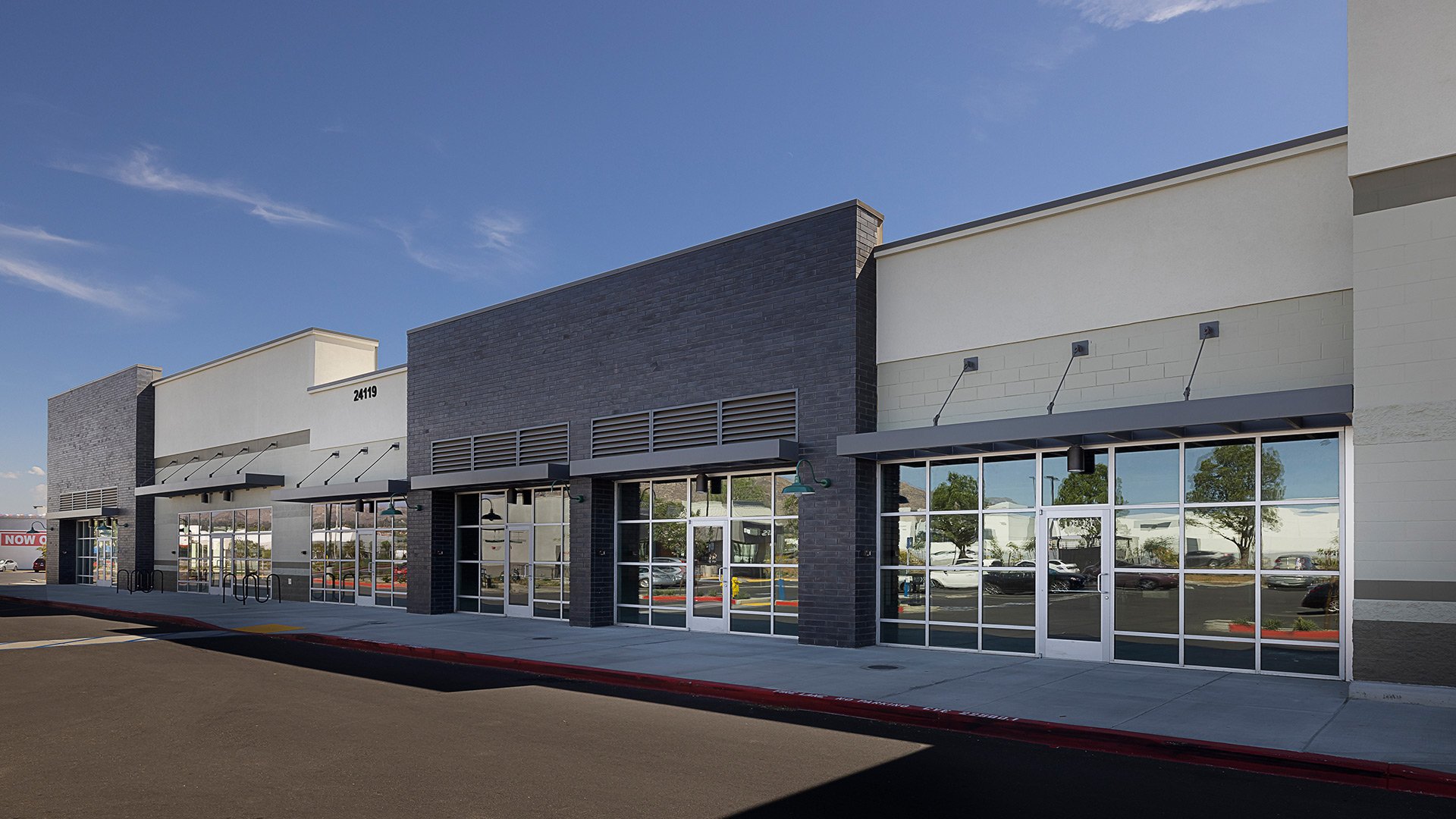 Modern shopping plaza with large glass windows, black and gray brick facade, and clear blue sky.