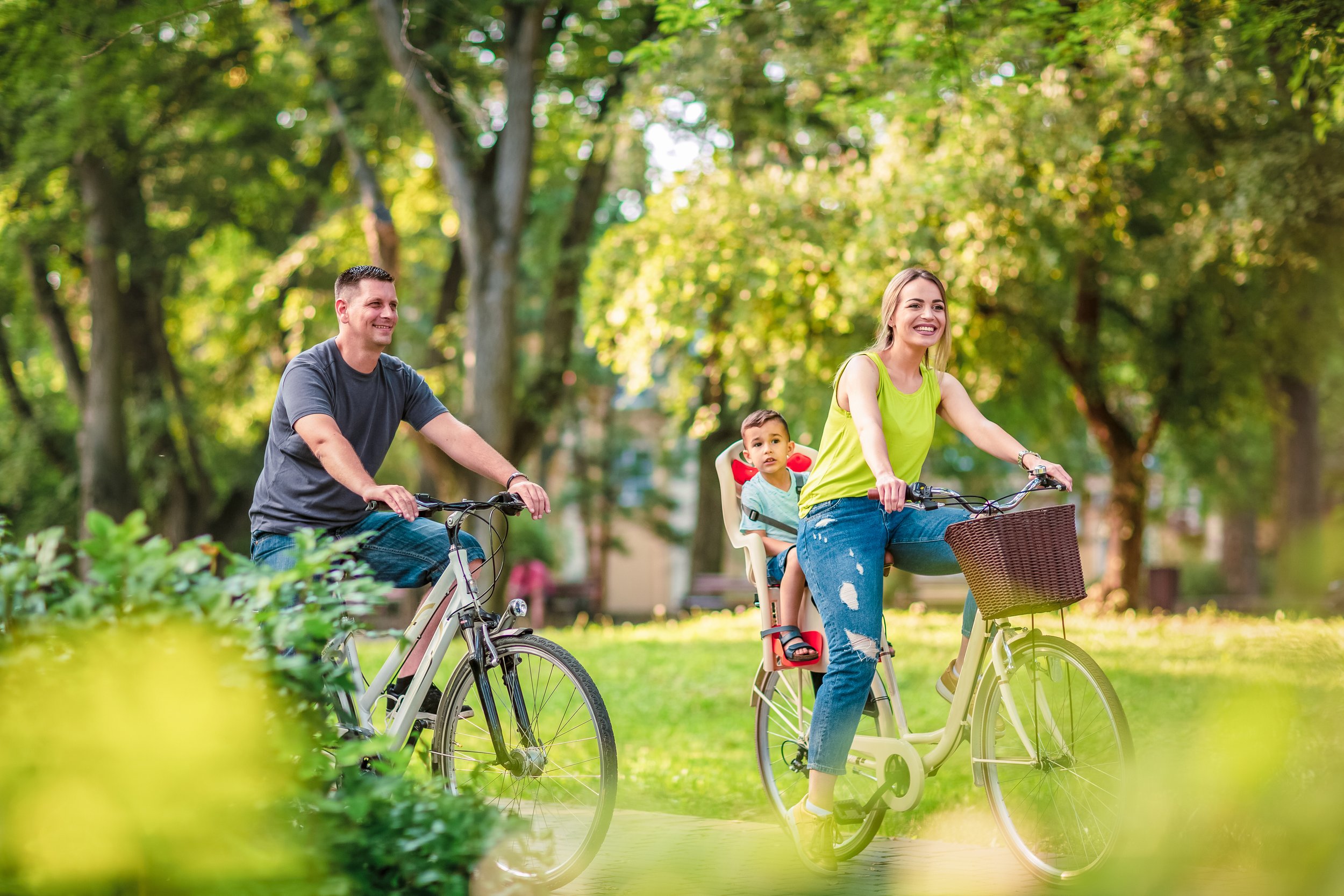 A family riding bikes in a park with trees in the background
