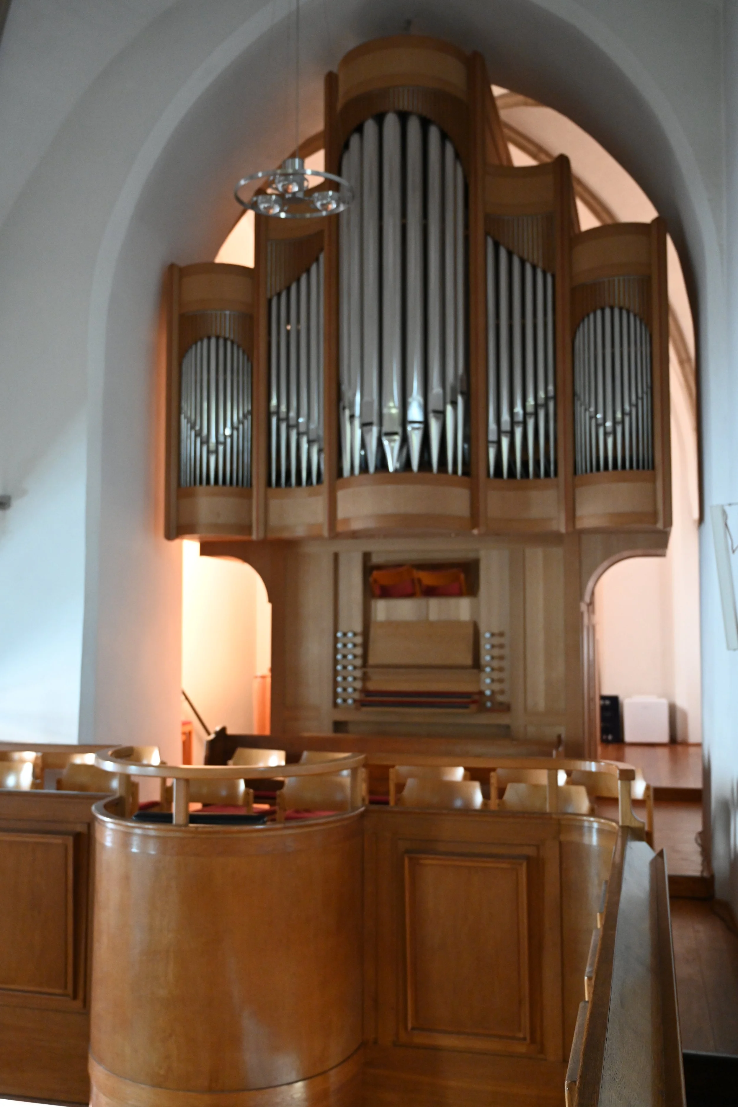 Innenraum einer Kirche mit einer großen Orgel aus Holz und Metall im Zentrum, umgeben von Holzbänken.