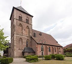 Eine alte Kirche aus rotem Backstein mit Turm und grünem Laub im Vordergrund