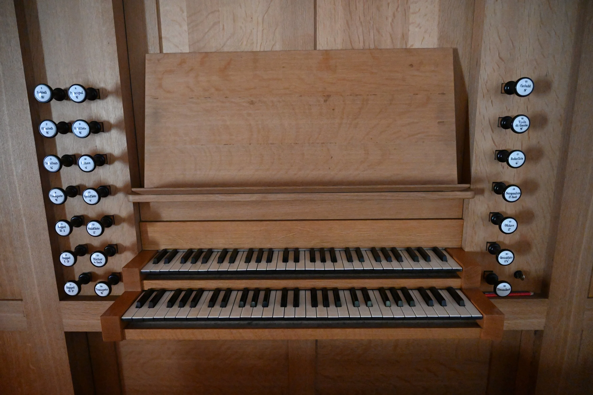 Ein hölzernes Orgelinstrument mit zwei Tastaturen und mehreren schwarzen Registern auf beiden Seiten.