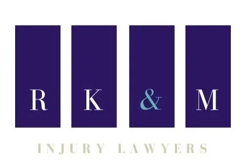 Logo with four dark blue vertical bars labeled R, K, &, and M, with the words "Injury Lawyers" underneath.